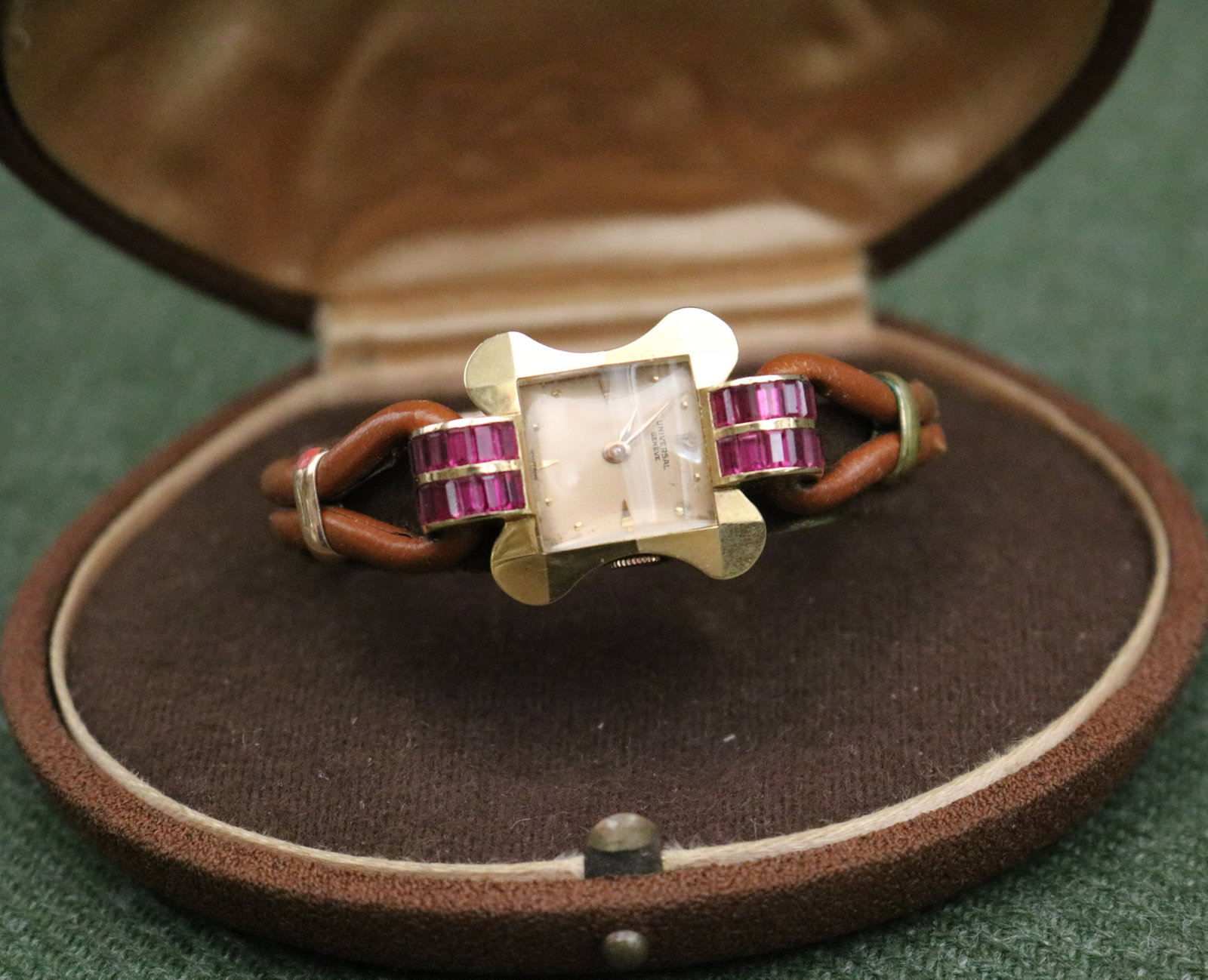 LADY'S 1940s 14K BRIGHT-POLISHED YELLOW GOLD AND RUBY WRISTWATCH BY UNIVERSAL, GENEVE - .: LADY'S 1940s 14K BRIGHT-POLISHED YELLOW GOLD AND RUBY WRISTWATCH BY UNIVERSAL, GENEVE Faceted, stylized quatrefoil case centered by four domed bars of total of 28 matched rectangular baguette rubies; 
