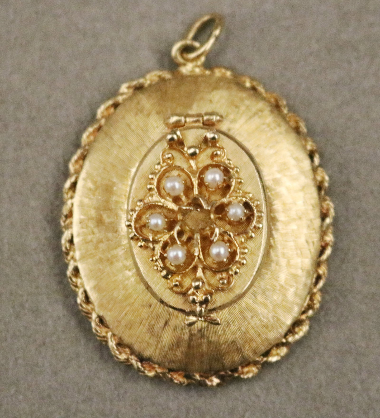 14K TEXTURED YELLOW GOLD AND SEED PEARL OVAL LOCKET - L: 1 5/8". Gross wt: 13 dwt..: 14K TEXTURED YELLOW GOLD AND SEED PEARL OVAL LOCKET Slightly domed locket with rope-twist border and openwork back panel, centers hinged panel set with six matched seed pearls surrounding space for ad