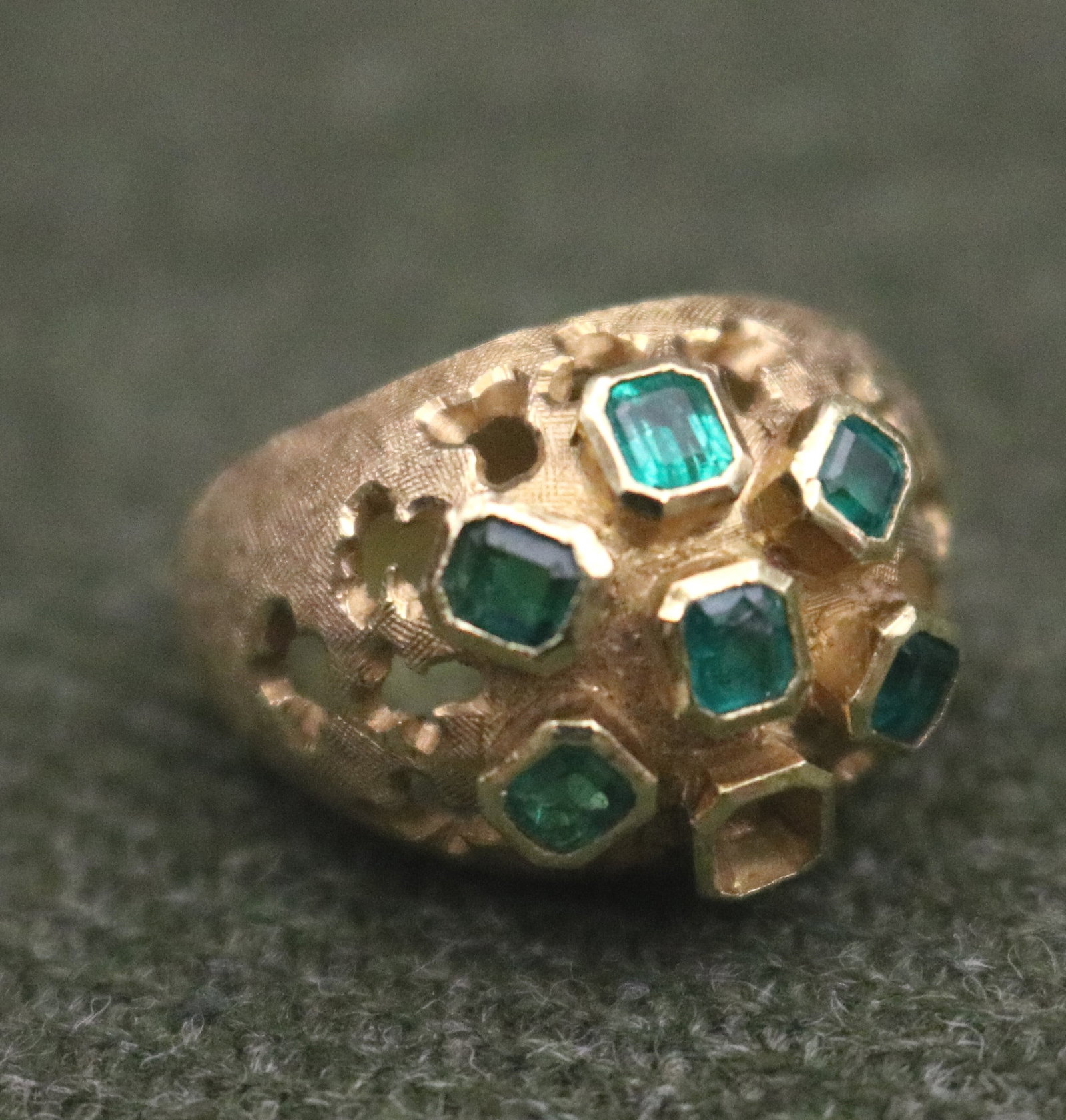18K TEXTURED YELLOW GOLD AND EMERALD DOME RING - Ring size: 5 3/4. Gross wt: 7 dwt..: 18K TEXTURED YELLOW GOLD AND EMERALD DOME RING Cluster of six matched rectangular emeralds each raised in bezel on pierced and textured dome Ring size: 5 3/4. Gross wt: 7 dwt.