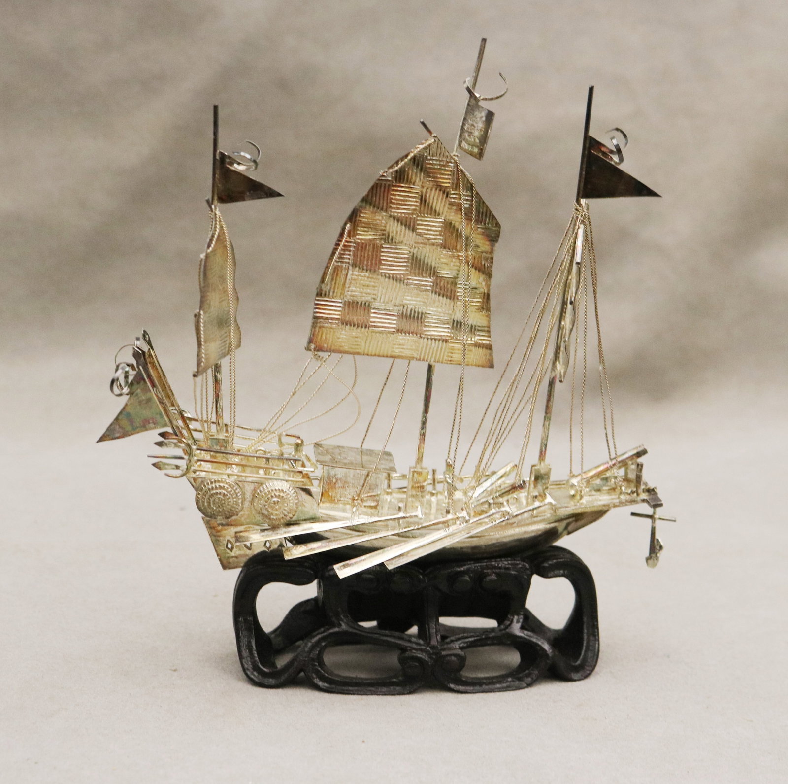 CHINESE STERLING SILVER MODEL OF WAR JUNK Made in Hong Kong - H: 6 3/4 in. Wt. 3.2 troy oz..: CHINESE STERLING SILVER MODEL OF WAR JUNK Made in Hong Kong Realistically modeled with cannons, figure on deck, movable rudder and anchor suspended on chain. On teakwood stand within glass-sided