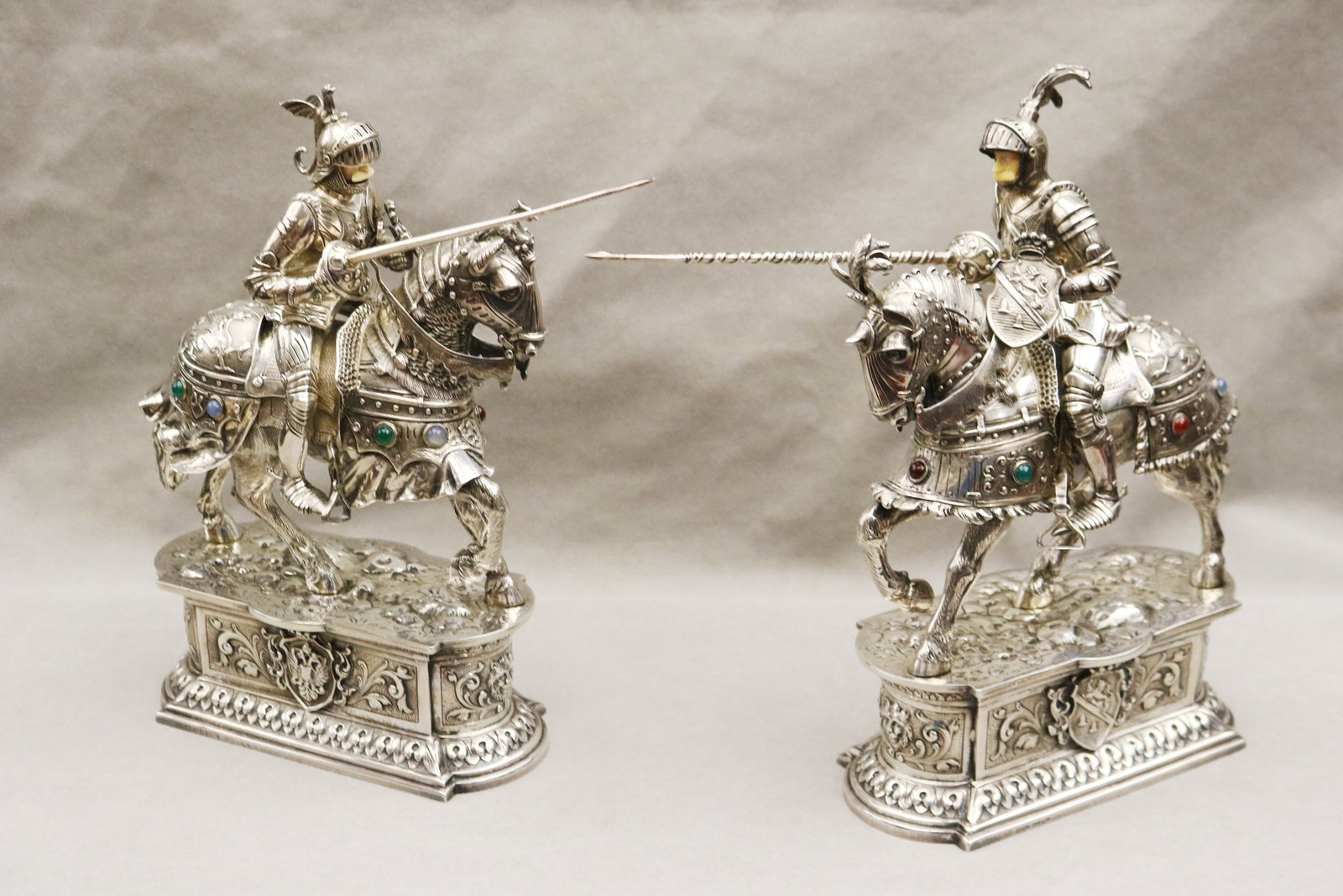 PAIR STERLING SILVER FIGURES OF JOUSTING KNIGHTS ON HORSEBACK, INSET WITH COLORED HARDSTONE GEMS: PAIR STERLING SILVER FIGURES OF JOUSTING KNIGHTS ON HORSEBACK, INSET WITH COLORED HARDSTONE GEMS late 19th/early 20th century Marked "Germany Sterling". Realistically modeled as knights with sculpted