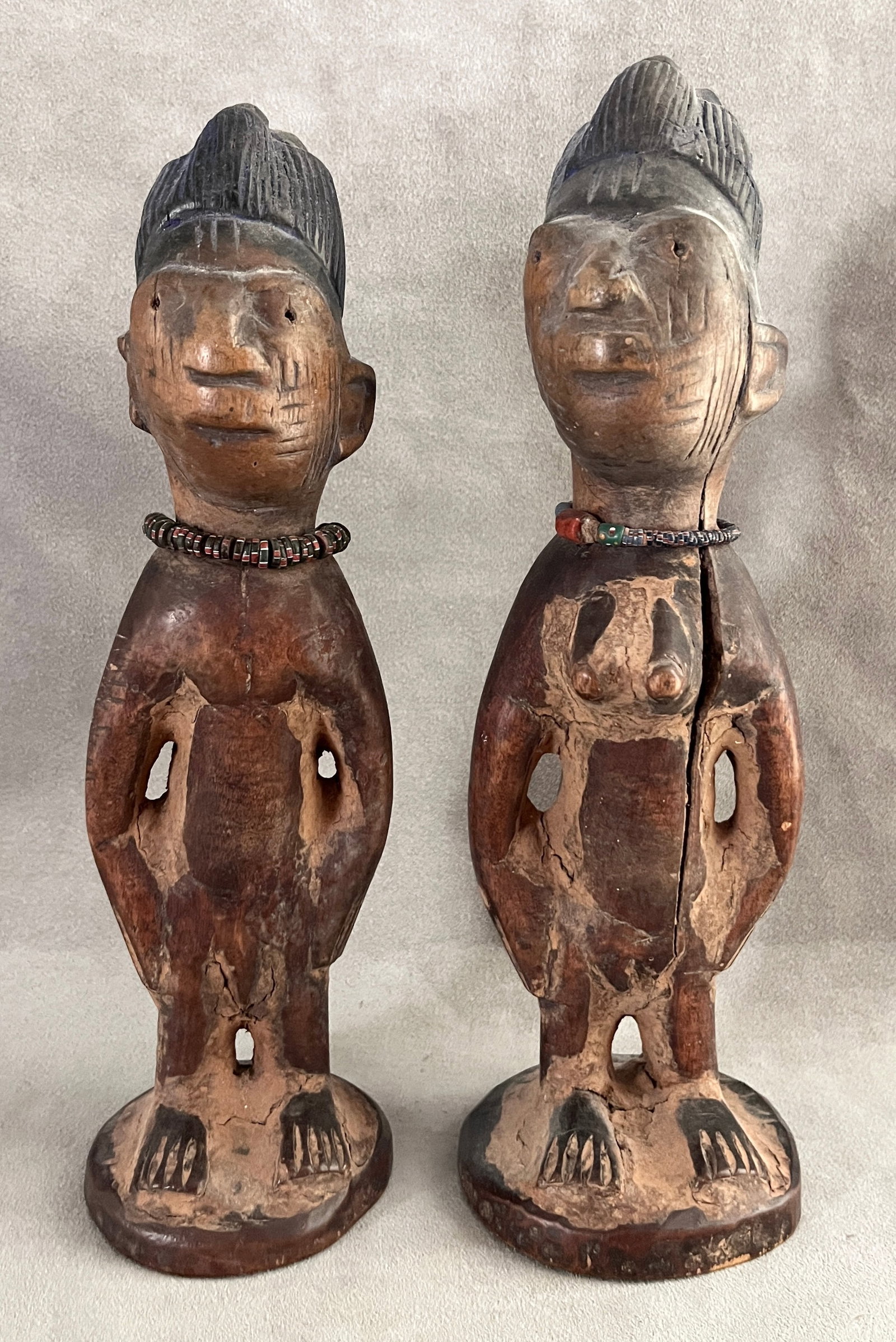 NIGERIAN PAIR OF YORUBA IBEJI TWIN MEMORIAL FIGURES - Height: 11.5 inches (tallest statue).: NIGERIAN PAIR OF YORUBA IBEJI TWIN MEMORIAL FIGURES Patinated pair of carved wood ibeji figures (a male and a female) from the Yoruba peoples of Nigeria, each standing on a rounded base with the chara