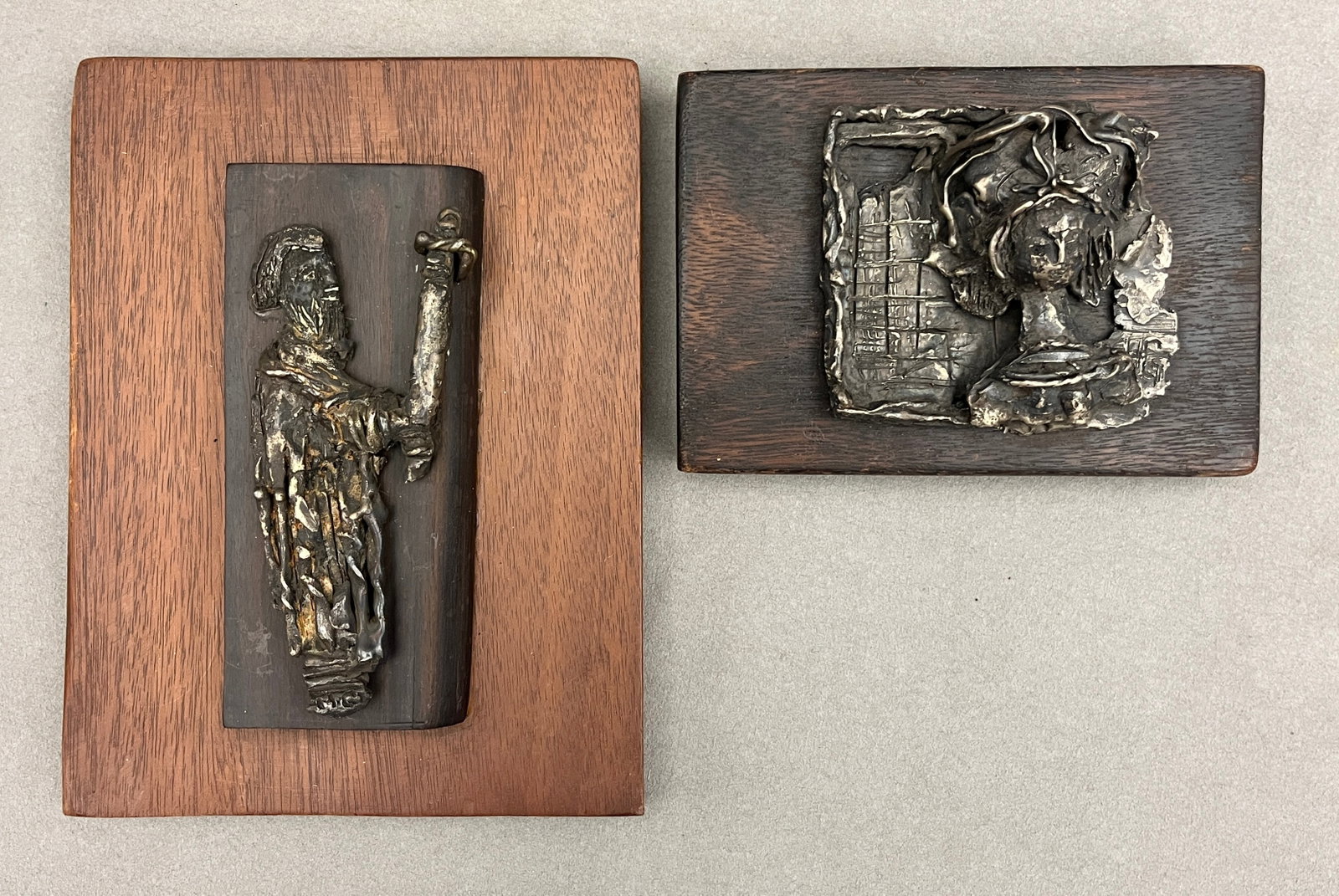 HANA GEBER (American, 1910-1990). Two Works: "Figure with Staff" and "Woman at the Lattice", Metal,: HANA GEBER American, 1910-1990 Two Works: "Figure with Staff" and "Woman at the Lattice" Metal A pair of textured cast white-metal relief plaques mounted on stained oak panels, depicting stylized robe