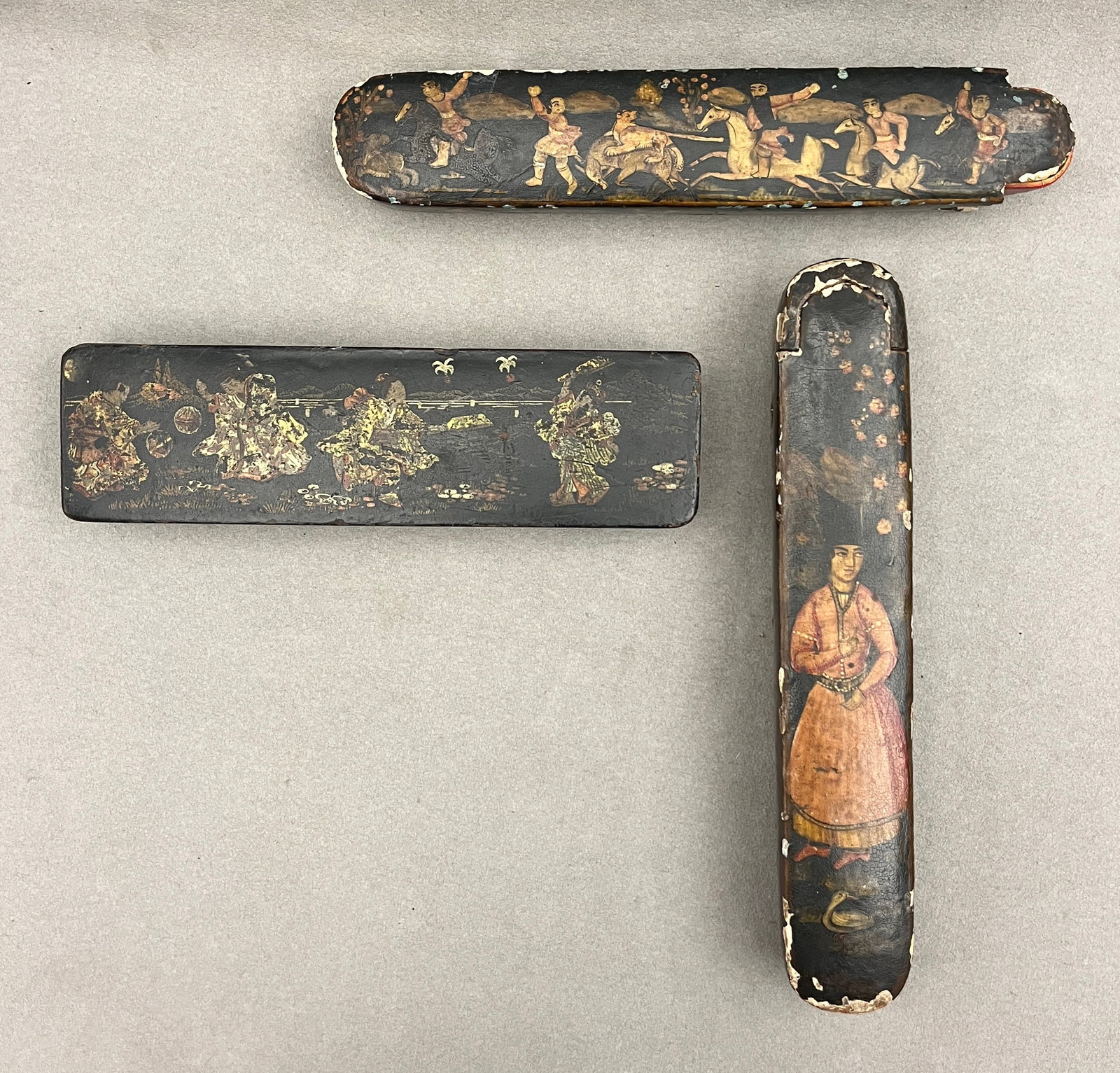GROUP THREE PERSIAN QAJAR AND ASIAN LACQUERED PAPIER-MACHE PEN CASES (QALAMDAN) - Largest, L: 9 in..: GROUP THREE PERSIAN QAJAR AND ASIAN LACQUERED PAPIER-MACHE PEN CASES (QALAMDAN) Embellished with polychrome and gilt decoration. First depicts Qajar hunting or courtly equestrian scenes; second depict