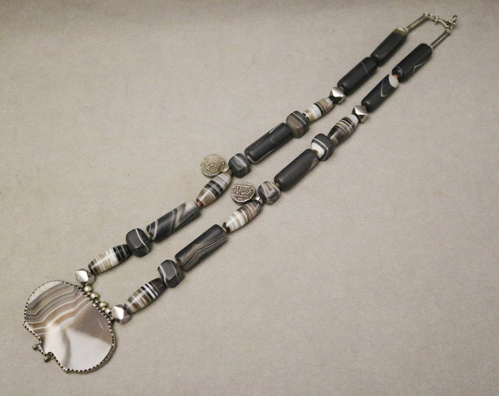CONTEMPORARY ARTISAN-CRAFTED NECKLACE BY ROSALEE COHEN DAVISON - L: app. 30 in. Medallion, W: 2: CONTEMPORARY ARTISAN-CRAFTED NECKLACE BY ROSALEE COHEN DAVISON Bezel-set central stone specimen medallion flanked by striped and banded cylindrical and cushion-form stone or agate beads with metal spa