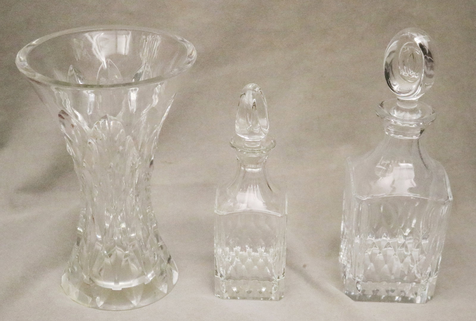 THREE COLORLESS CARTIER CRYSTAL TABLE ITEMS - Vase, H: 10 in..: THREE COLORLESS CARTIER CRYSTAL TABLE ITEMS Each logo signed. Two graduated square-sided decanters and flaring vase Vase, H: 10 in.