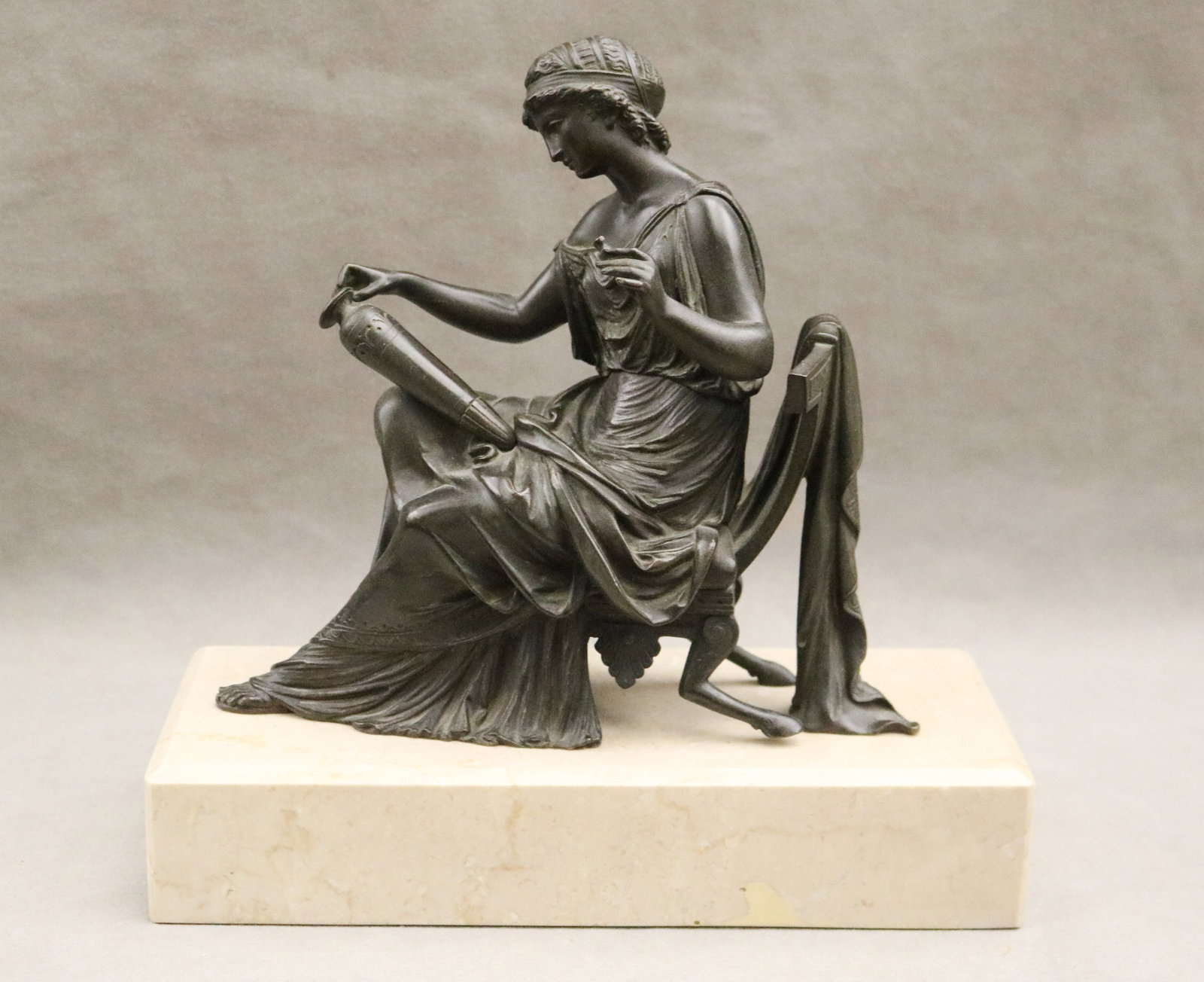 AFTER LEON PILET (French, 1836-1916). NEOCLASSICAL BRONZE FIGURE CAST AS SEATED GODDESS ADMIRING: AFTER LEON PILET French, 1836-1916 NEOCLASSICAL BRONZE FIGURE CAST AS SEATED GODDESS ADMIRING URN On marble On cream color marble rectangular base. Black patina Overall, H: 11 in. Base, 11 in. x 4