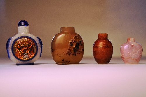 A collection of four C19th Chinese snuff bottles includ: A collection of four C19th Chinese snuff bottles including a gilded silk painted beneath glass overlay panel a Chalcedony carved bird on a branch and a lavender jadeite with prunus and a russet jadeit