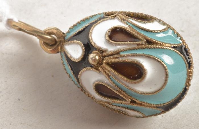 An enamelled Russian egg pendant, the egg with wh: An enamelled Russian egg pendant, the egg with white, light blue, black and brown enamelling, with Kokoshnik mark and '925', late 20th century, 2.8cm longIMPORTANT: This lot is subject to VAT and the