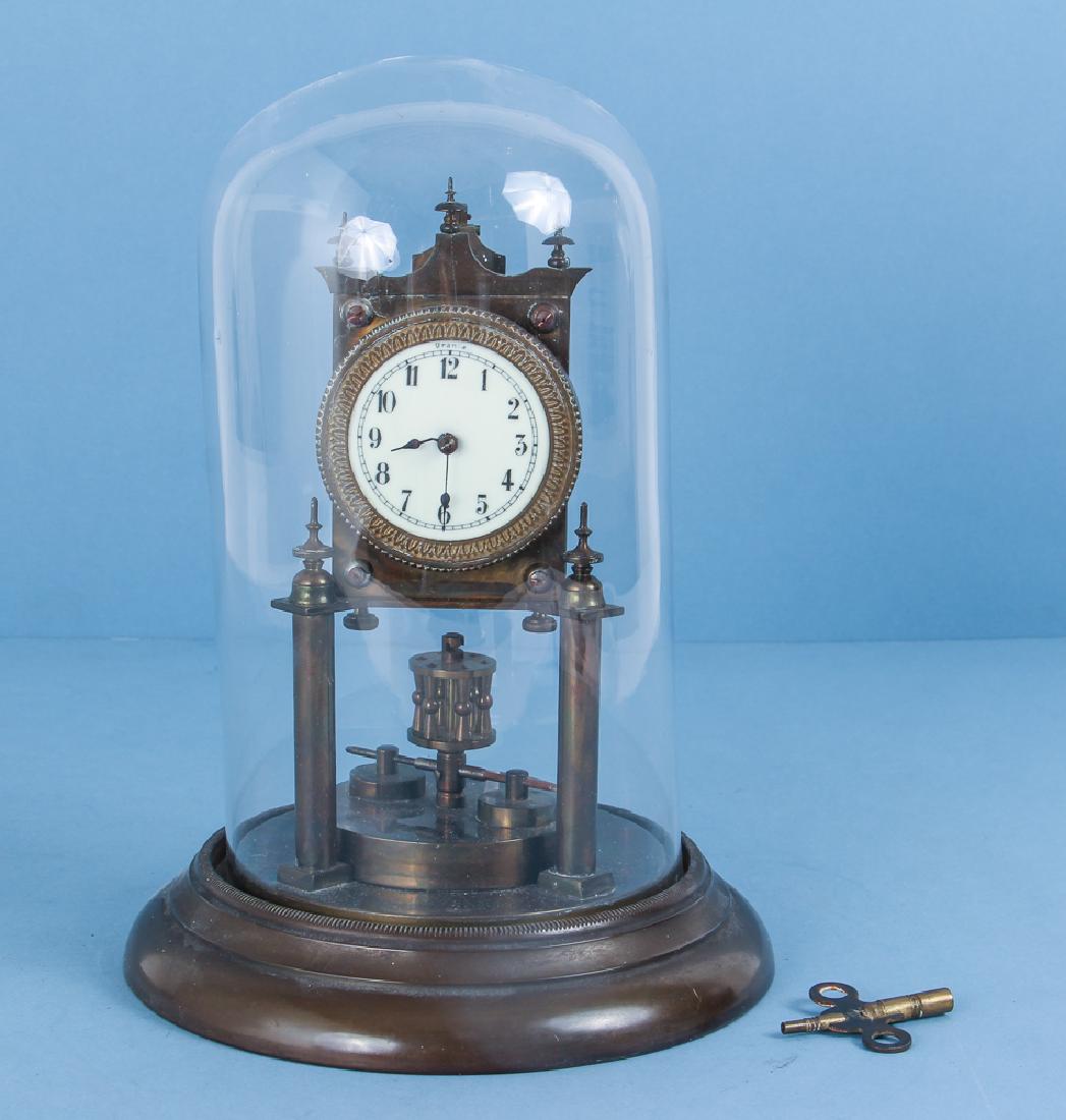 English Brass Urania Anniversary Clock: English brass Urania anniversary clock, under glass dome, measuring 11 by 7 inches. Estate of Roberta Watson Odell.