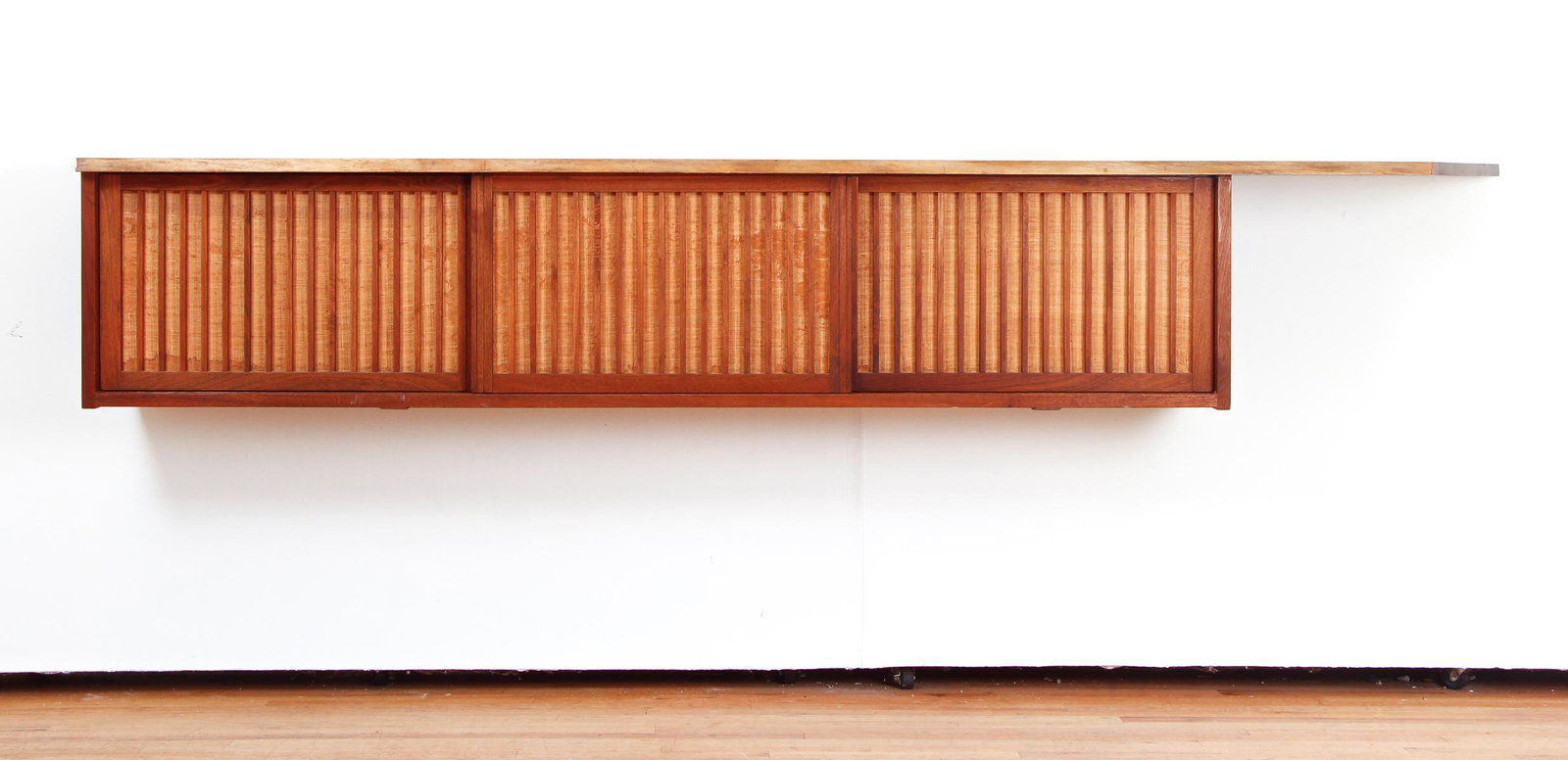 George Nakashima Walnut Cantilevered Free Edge Credenza: George Nakashima cantilevered free edge credenza, walnut, three door with pandanus covering, adapted as a sheet music cabinet, measuring 108 by 18 1/2 by 18 1/2 inches.