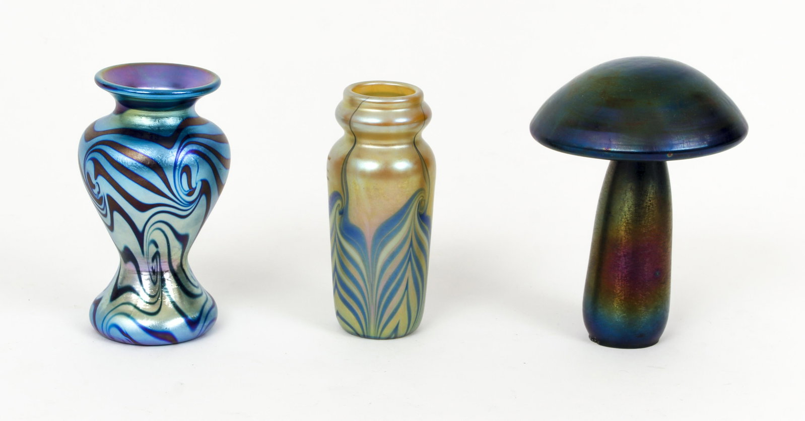 3 Iridescent Art Glass Mushroom Vases Lundberg: Lot of 3 pieces of iridescent art glass, two vases (one by Lundberg and one by Carlson) and one mushroom marker L 02 on base, all right around 4.5 inches tall. Provenance: The Estate of Charles M. Die