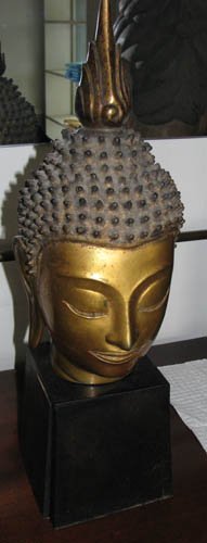 Polished Bronze Buddha Head: Title: Polished Bronze Buddha Head on wood stand Medium: bronze Dimensions: 22 x 7 x 7 inches The Estate of Shirley Burke