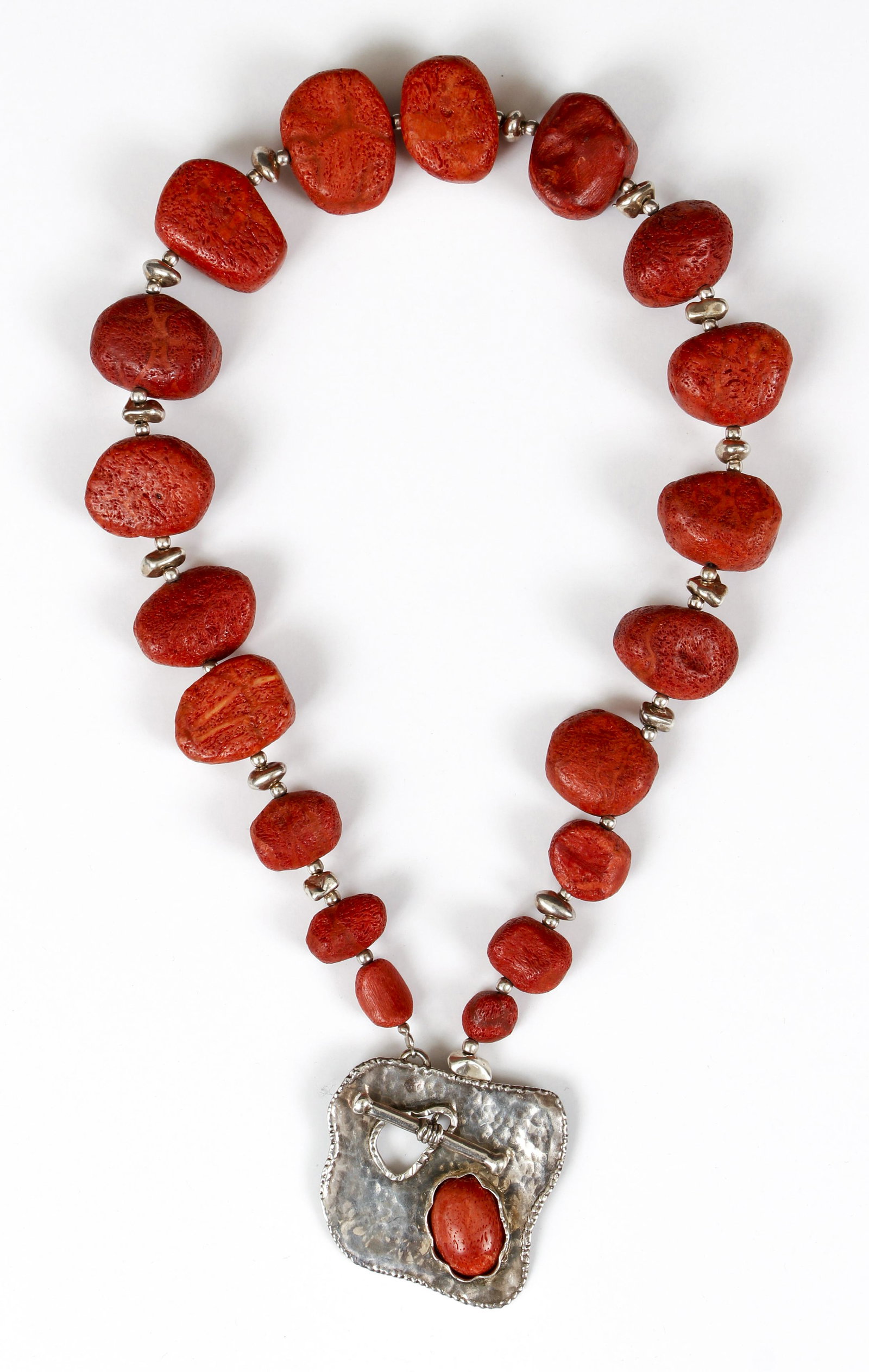 Contemporary Sterling Coral Necklace: Contemporary silver and coral necklace fashioned of barely polished coral stones and silver beads. The porous appearance of the coral is combined with chunky silver beads and amorphic hammered pendant