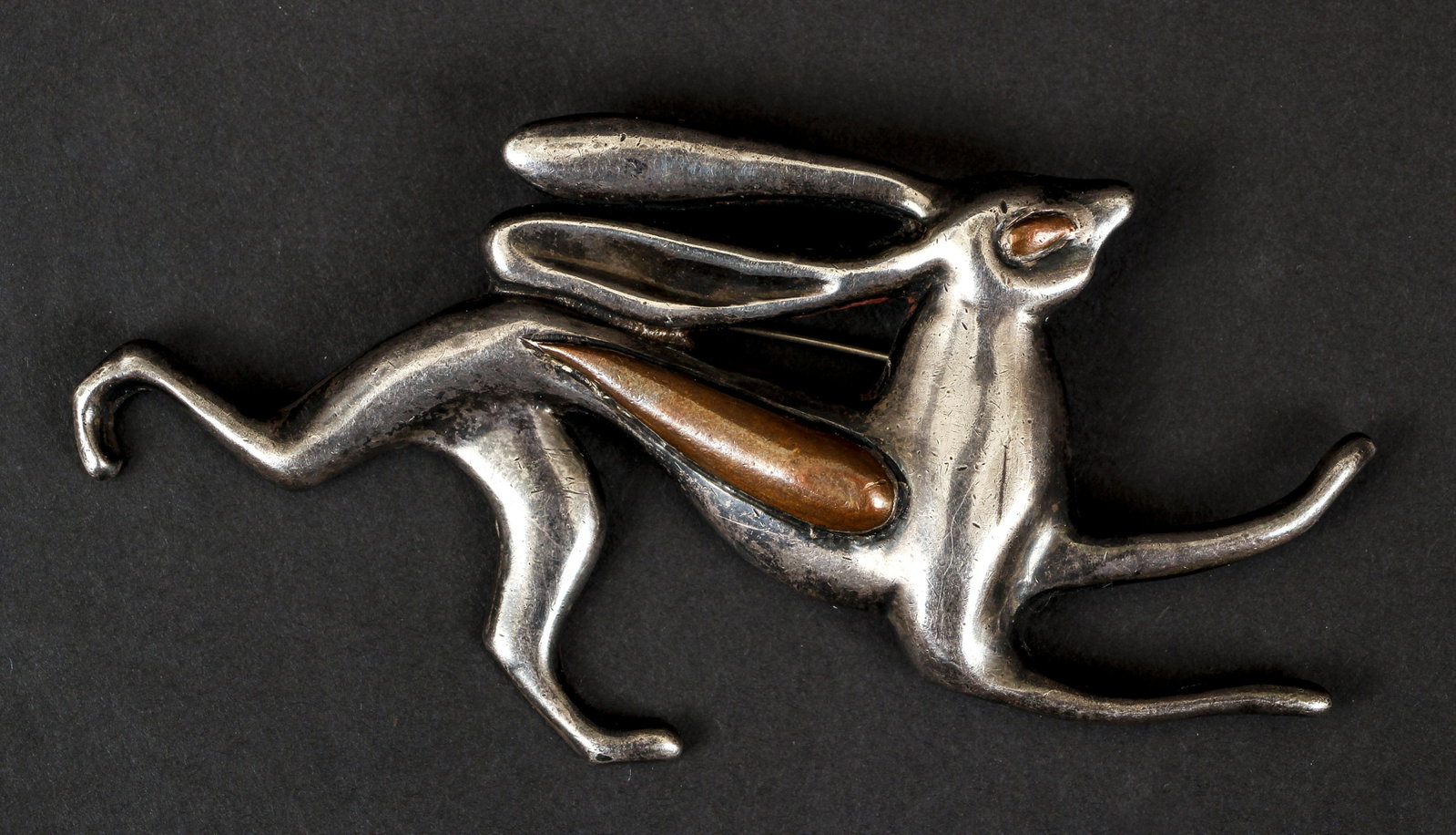 Silver Taxco Rabbit Pin: Silver Taxco rabbit pin. The large pin is fashioned in the shape of a bounding rabbit. The figure is exaggerated in design with long flowing ears and stretched out legs. Details of copper metal make u