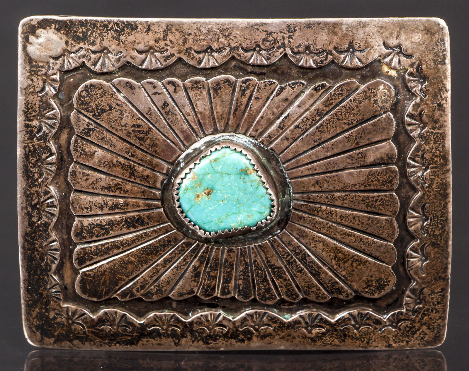 Silver Turquoise Belt Buckle: Silver turquoise belt buckle. The rectangular buckle is engraved with a central radiating figure bezel set with a polished turquoise stone. The edges of the buckle are finished with a scalloped frame 