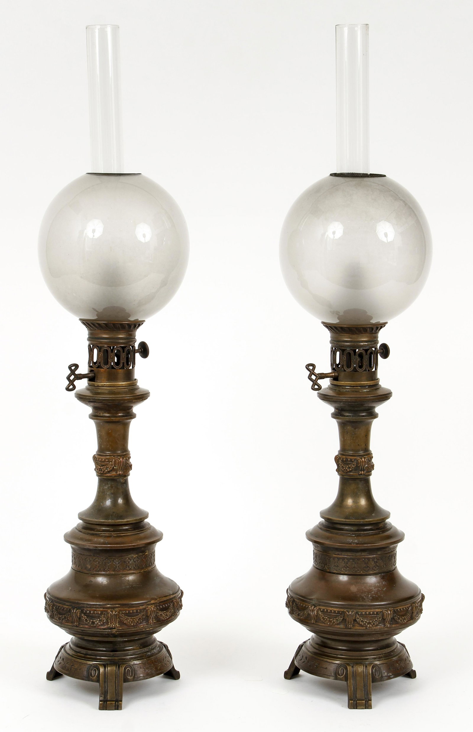 Pair of French Frosted to Clear Glass Metal Oil Lamps: Pair French oil lamps, late 19th c., including frosted glass shades, lamps decorated by swags and garlands in relief rising on lamp body, accented by metal ring at top and bottom, rising on metal body