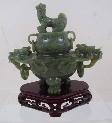 Carved Green Soapstone Chinese Koro: Title: Chinese Koro made from green soapstone on wooden carved base Medium: soapstone and wood Dimensions: 6.75 x 6 x 2.75 Description: carved spinach-green soapstone, foo dog finial on the lid, and f