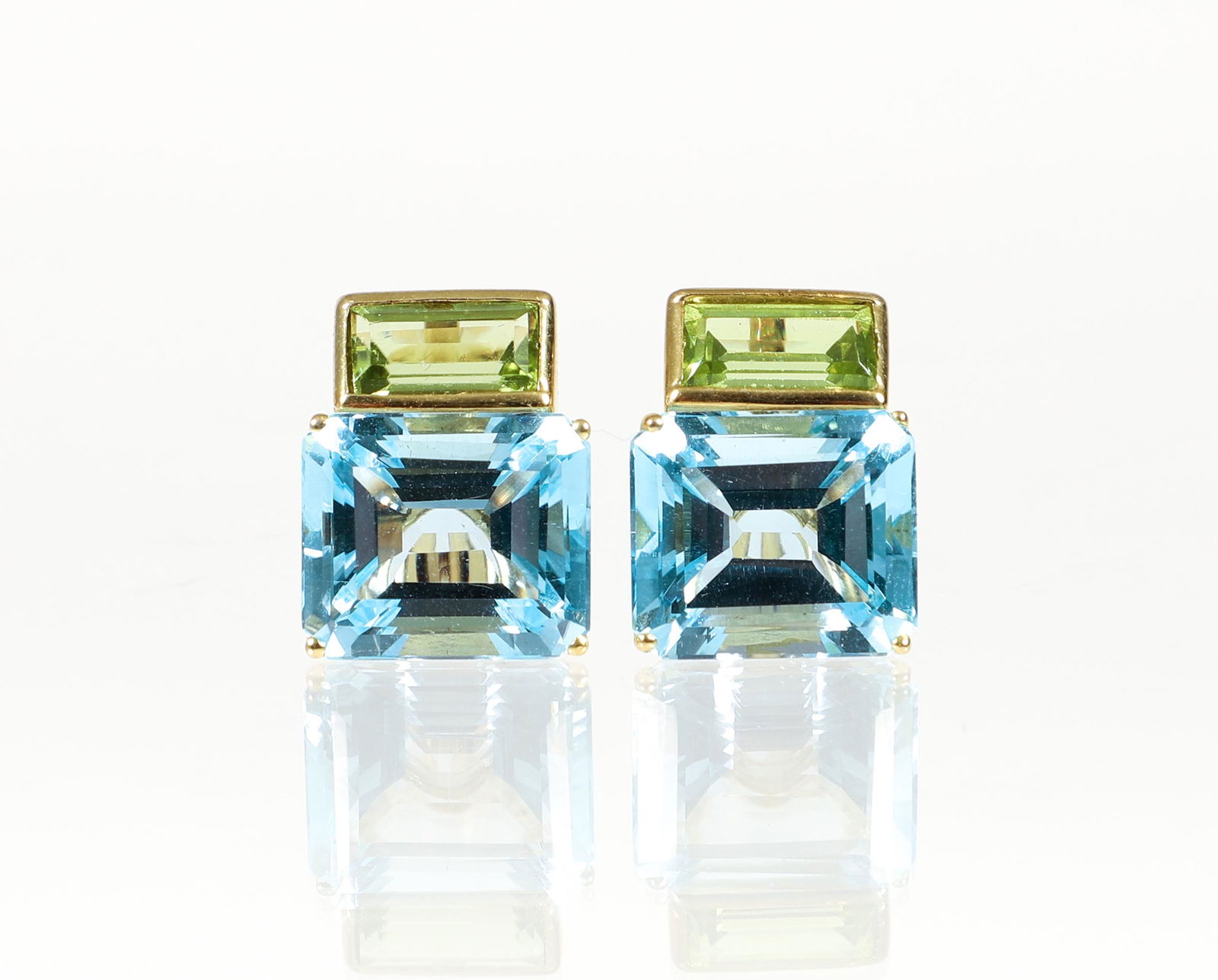 14K Blue Topaz Peridot Earrings: 14K yellow gold blue topaz & peridot clip earrings. The earrings are designed with a basket set blue topaz 14 x 12mm, and a bezel set peridot 9.5 x 6mm. Finished with clip backs. Marked "MAZ 14K". App