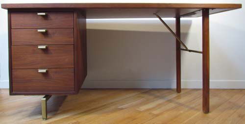 Trapezoidal Desk with white laminate top: Title: Trapezoidal white laminate top over 4 drawers of walnut laminate with brass pulls, drawers have adjustable sectional areas Date: circa 1954 Dimensions: 29.75 x 29.75 x 60 inches Signature: unla