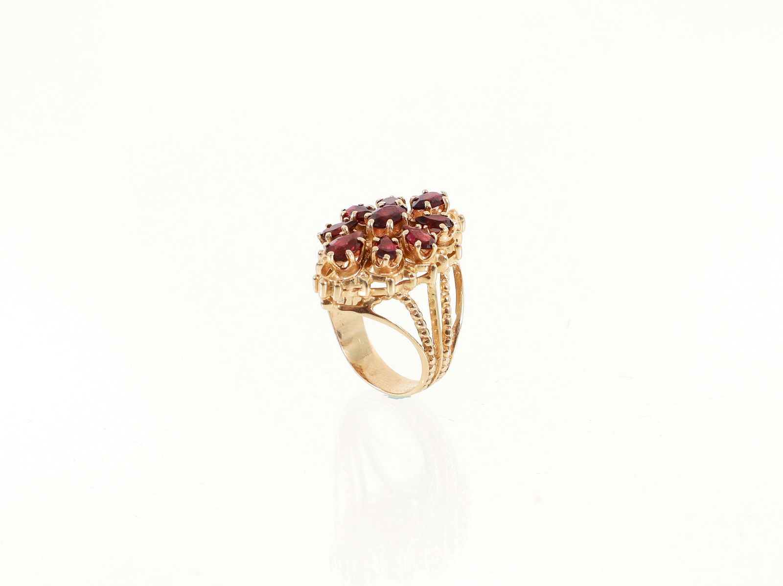 14K Floral Garnet Ring: 14K floral garnet ring. The band of this yellow gold ring is split into 5 stems that reach up to the scalloped face. Cutwork petals set with pear cut garnets surround an oval garnet at the center. The