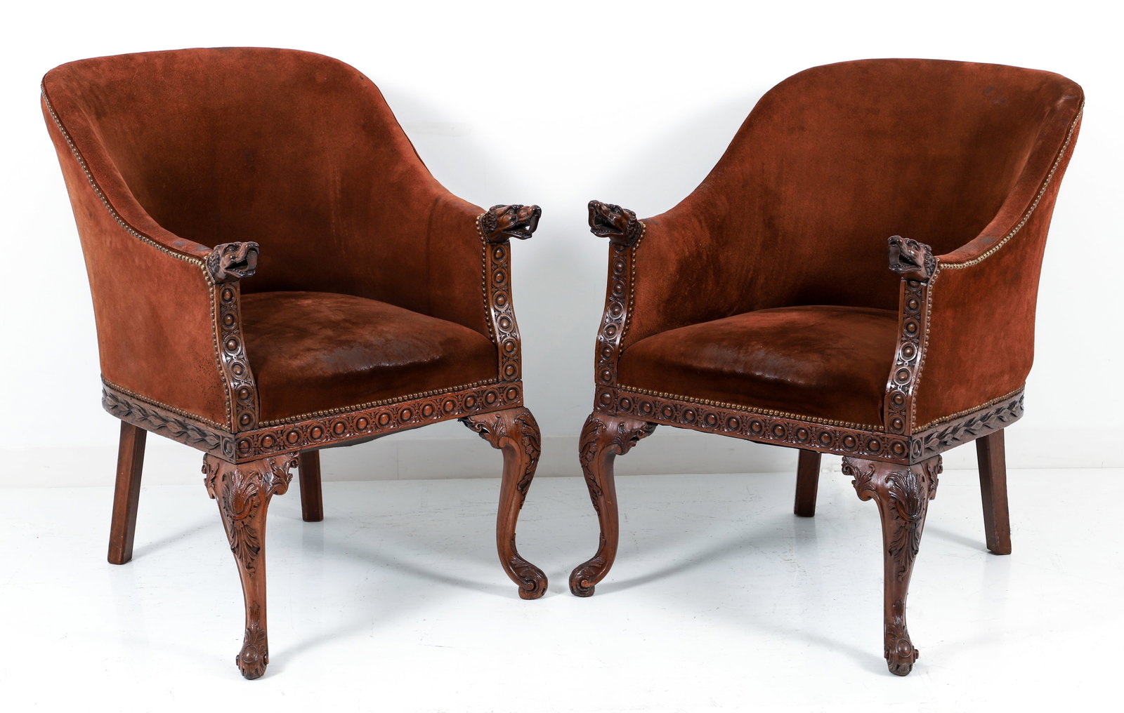 Pair of George II Highly Carved Bergeres: A pair of George II highly carved bergeres, mid 18th century. Reupholstered chairs in a rich chocolate suede with brass tack detailing. Barrel backs, arms ending in intricately carved hound/wolf/dog h