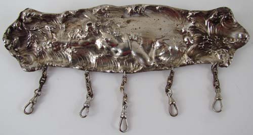 Chatelaine of a Silver Brush Cover: Title: Silver brush cover with image of Venus being washed ashore; 2 hooks for neck chain and 5 chain drops Medium: silver plate Dimensions: 7 x 2 inches Description: Basically tool kits masquerading 