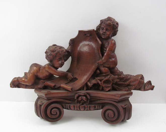 Architectural wall Bracket surmounted with Cherubs hold: Title: Architectural wall Bracket surmounted with Cherubs holding a Cartouche Date: 19th century Medium: carved walnut Dimensions: 19 x 26 x 6 inches Provenance: Mary McBride