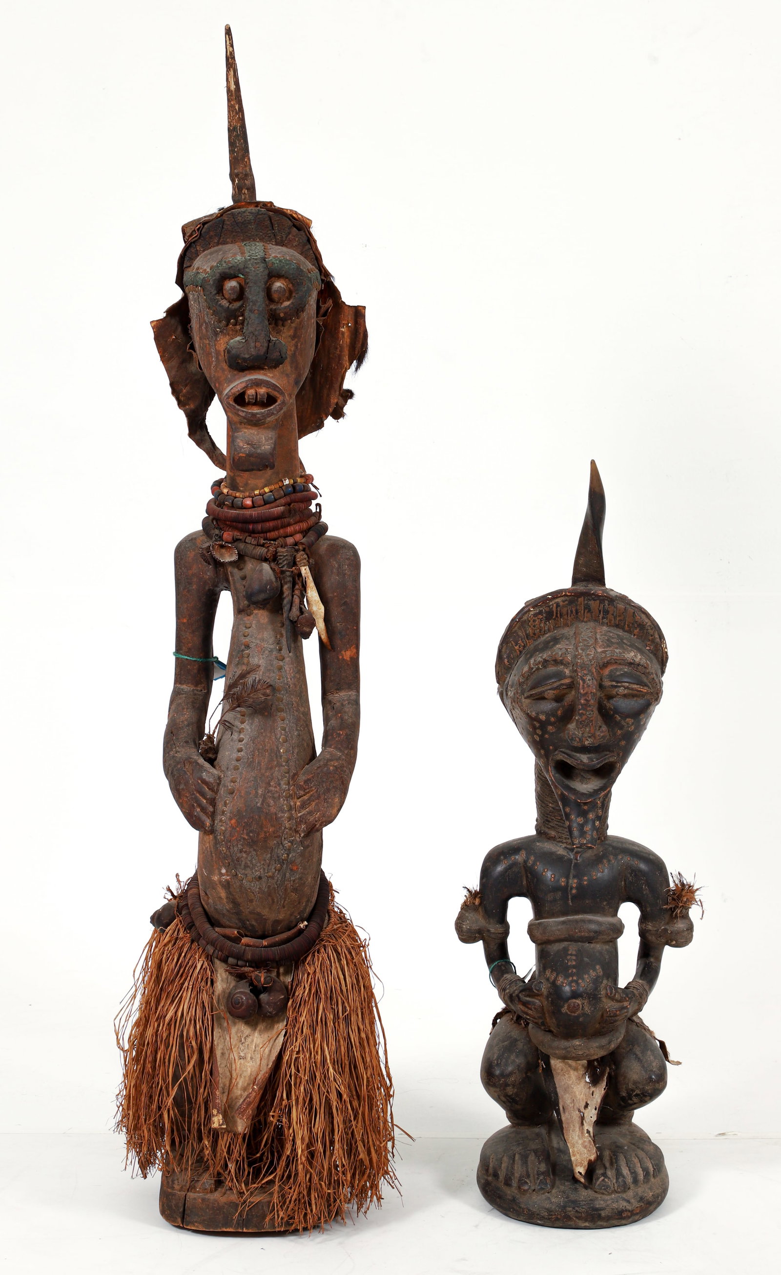 2 Songye Nkisi Power Figure: Nkisi power figure, Songye peoples (or after), Democratic Republic of the Congo. Large carved wood figure with copper attachments around the eyes, vulcanite beads, horn necklace, raffia skirt, magic