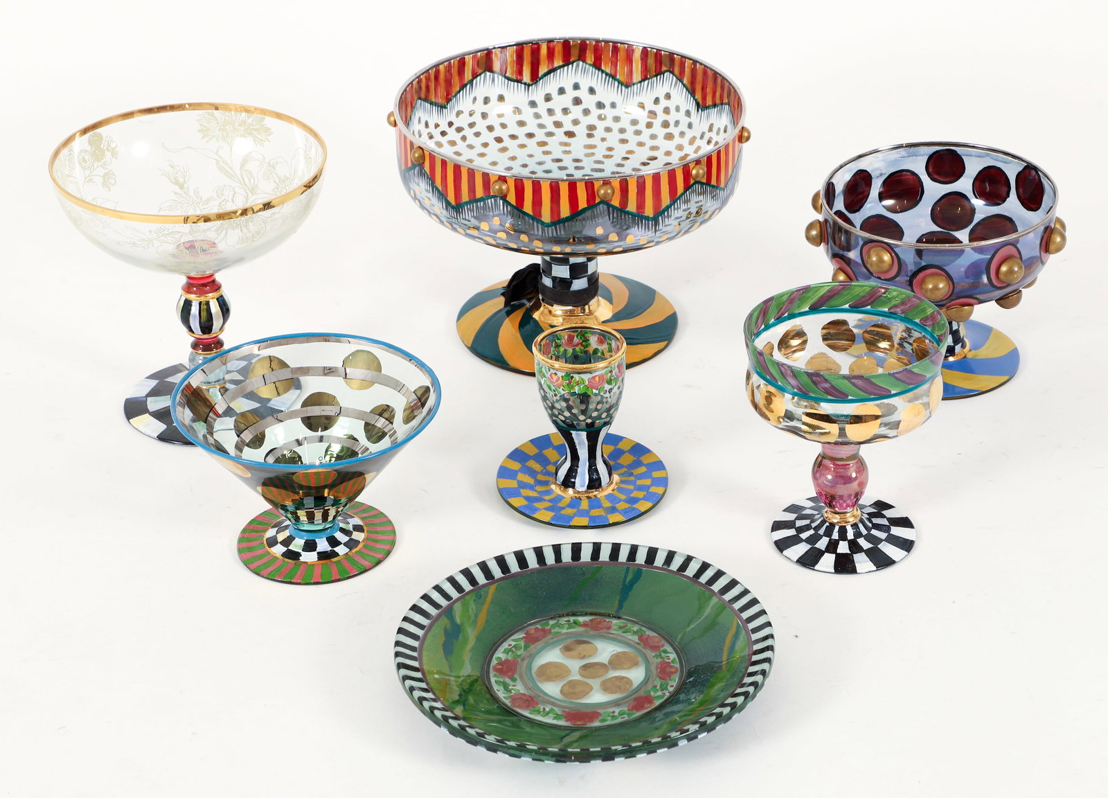 Group of 6 MacKenzie-Childs Handpainted Glass Pieces: Group of 7 MacKenzie-Childs handpainted glass pieces, American, 1990s. Includes: Large compote, coupes, martini glass, candle holder, and plate. Polka dot, checkered, and floral motifs throughout.