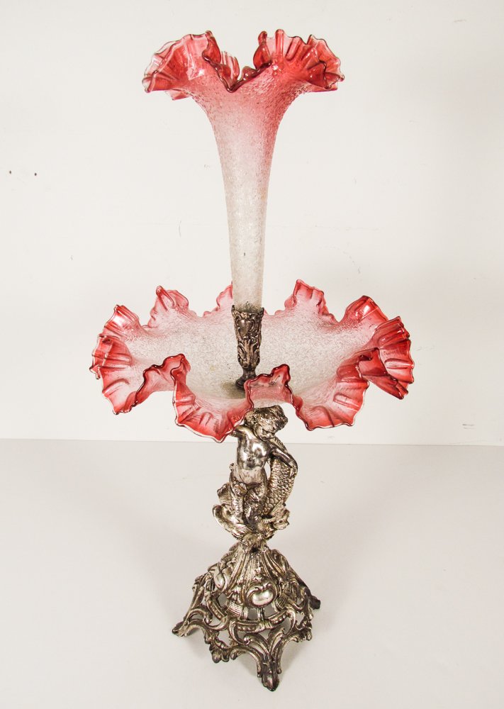 Late Victorian art glass and sculpted silver base: Title: Late Victorian art glass and sculpted silver base epergne, pink sandwich glass with silver aquatic cherub motif base Medium: glass and metal Dimensions: 23 inches tall, 12 inches in diameter Si