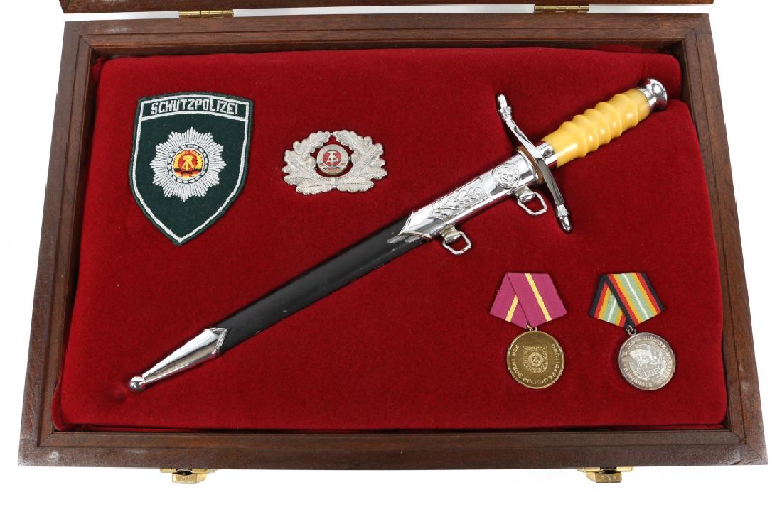 EAST GERMAN DRESS DAGGER WITH MEDAL & INSIGNIA LOT: EAST GERMAN DRESS DAGGER WITH MEDAL & INSIGNIA LOT 1- Cold War era, East German Officer dress dagger. Blade number # 75826. 1- Officer cap badge. 1- Police shoulder patch. 1- Lot of 2 medals. 1- woode