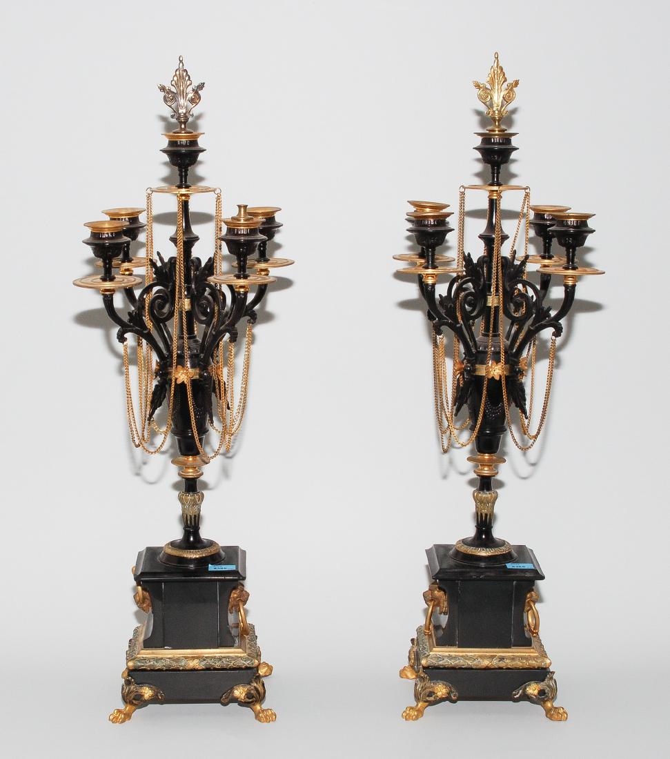 1 Paar grosse Girandolen Napoléon III. Messing, tlw.: 1 Paar grosse Girandolen Napoléon III. Messing, tlw. geschwärzt. 5-flammig. Mehrteiliger Balusterschaft. Rechteckiger Steinsockel mit seitlichen Löwenköpfen auf 4 Tatzenfüsschen. Geschwungene Leu