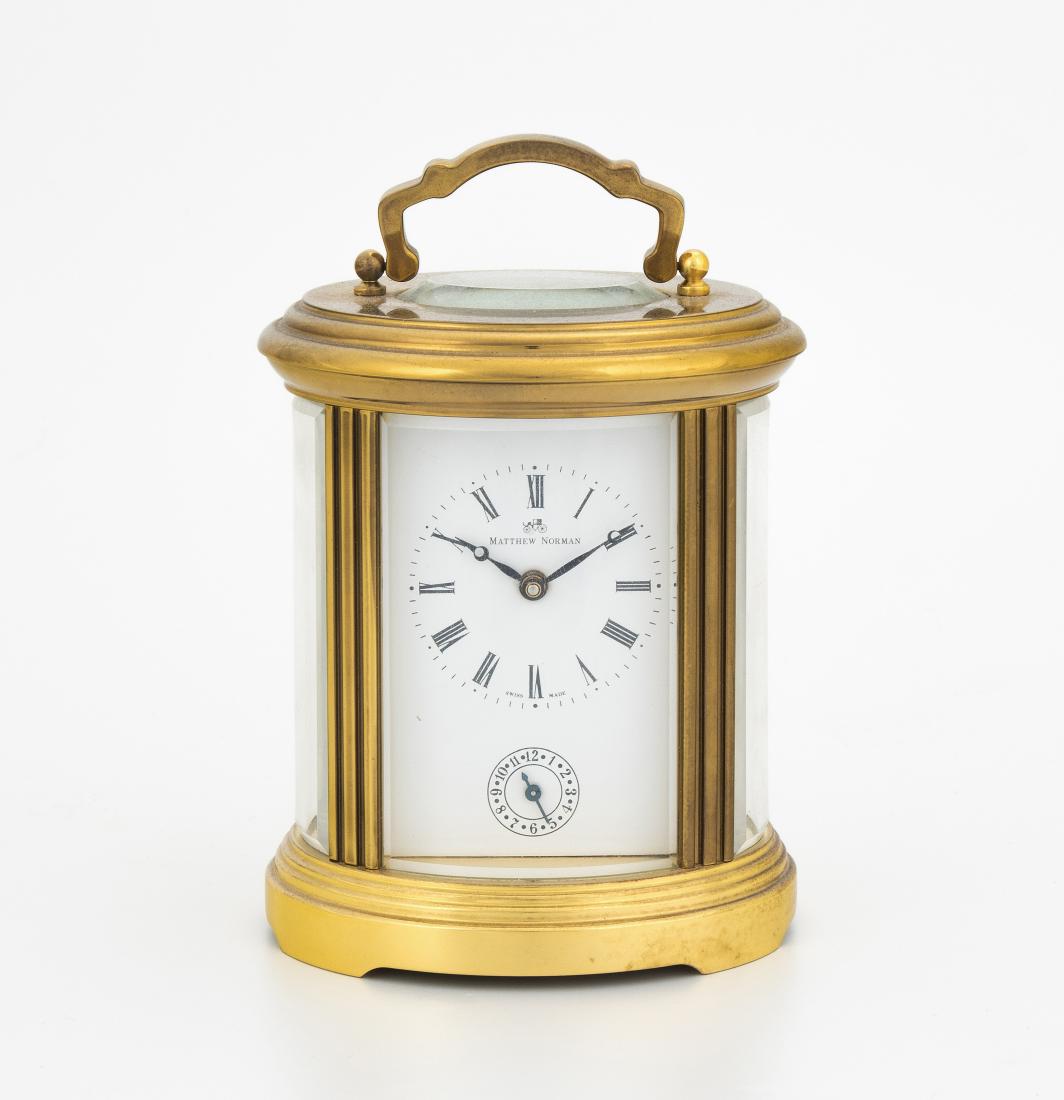 Reisewecker Matthew Normann: Schweiz, 20.Jh. Allseitig verglastes, vergoldetes Messinggehäuse mit Traggriff. Weisses Zifferblatt mit römischen Zahlen und Signatur "Matthew Normann". Weckanzeige bei 6 Uhr. Unruhewerk mit Weckerf