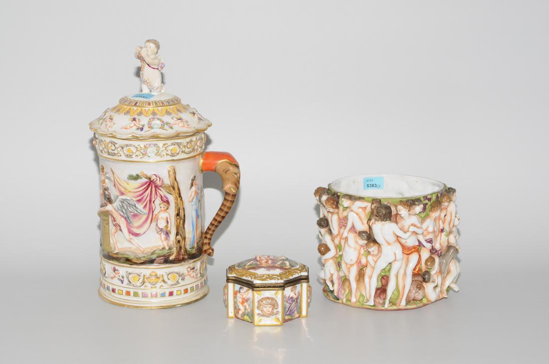 Lot: 3 Porzellangefässe: Capodimonte, 19.Jh. Porzellan. Reliefdekor mit antiken Szenen in polychromer Malerei und mit Goldstaffierungen. Bezeichnet: N unter Krone. Bestand: Deckelkrug. H 31 cm. Cachepot, H 13,5 cm. Deckeldose