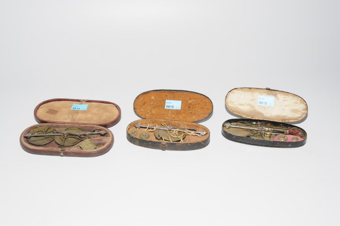 Lot: 3 kleine Münzwaagen: England, um 1800 bzw. 1.Hälfte 19.Jh. Balkenwaage aus Eisen mit Schalen und Gewichten aus Messing. In Original-Schatulle aus Metall bzw. braun beledertem Holz. 1 mit geprägter Deckelmarke: "W&T. AVE
