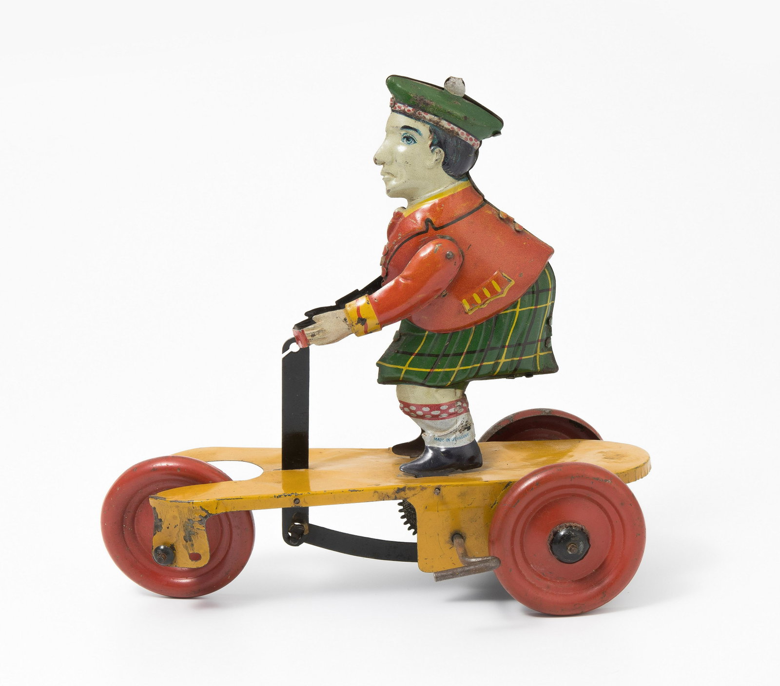 Günthermann-Figur "Schotte auf Roller": Deutschland, um 1930. Mit Firmensignet. Bezeichnet: "MADE IN GERMANY". Blech, farbig lithographiert. Schotte in Kilt auf gelbem Roller mit 3 roten Rädern. Uhrwerkantrieb. L 17,5 cm. - Bespielt. Klein