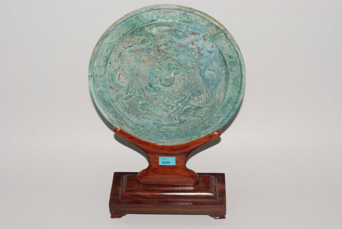 Handspiegel China, in der Art der Tangâ€“Dynastie.: Handspiegel China, in der Art der Tangâ€“Dynastie. Bronze. Rundform. RÃ¼ckseite mit Knauf in BlÃ¼tenform umgeben von reliefierten Drachen. GrÃ¼n patiniert. Riss am Rand. D 22,5. Auf Holzsoc