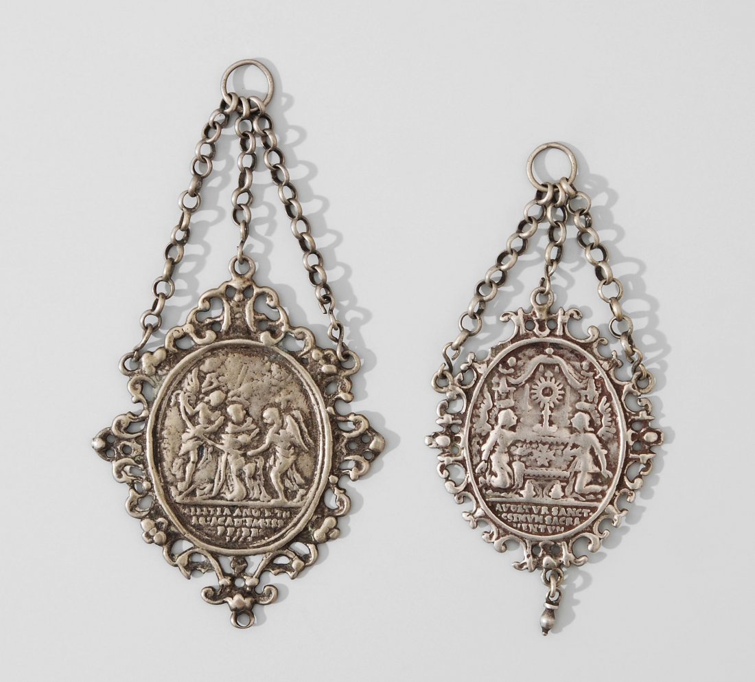 Lot: 2 Tauf-Medaillons Wohl deutsch, Ende 18.Jh.: Lot: 2 Tauf-Medaillons Wohl deutsch, Ende 18.Jh. Versilbert. Ovale Medaillons mit durchbrochen gearbeiteter Umrahmung. Anhängeöse an 3 Kettchen. Reliefierte Darstellung eines Altars mit 2 Engeln bzw