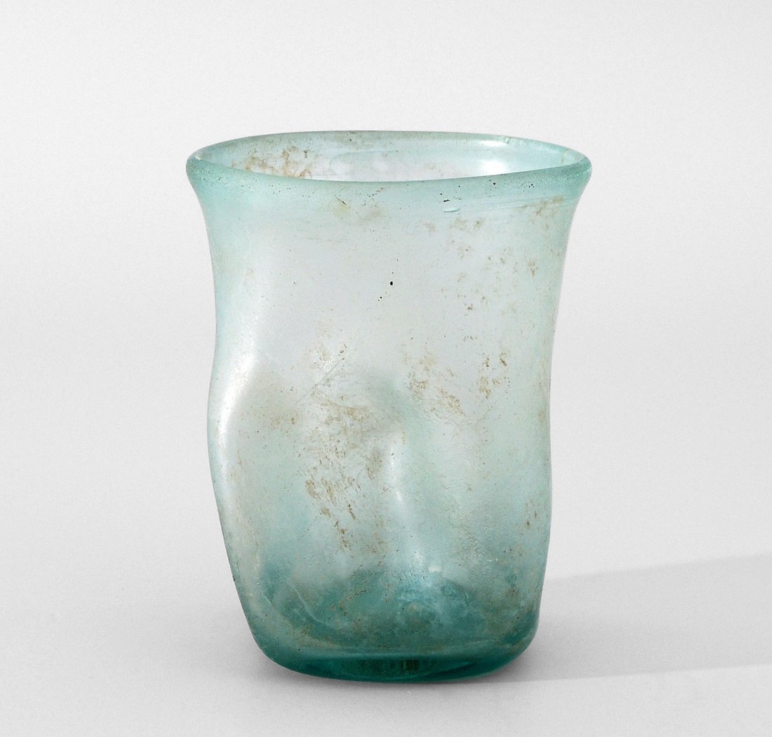 Becher Östlicher Mittelmeerraum, vermutlich 2.Jh. n.: Becher Östlicher Mittelmeerraum, vermutlich 2.Jh. n. Chr. Leicht bläuliches Glas. Geradwandig, vierfach eingedellt. Boden Konkav. Verdickter Rand. Verwittert. H 8,7, D 6,6 cm.