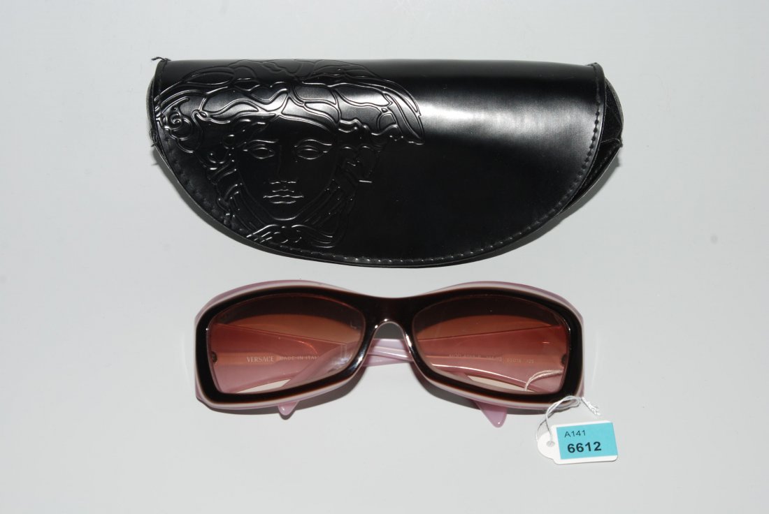Versace, Sonnenbrille Brauner und mauvefarbener: Versace, Sonnenbrille Brauner und mauvefarbener Kunststoff. Bgel mit Strass verziert (vier Strasssteinchen fehlen). In Original-Etui. Bgellnge 12 cm, H 4,7 cm, B 15 cm. Gebrauchsspuren. Glser mit Korr
