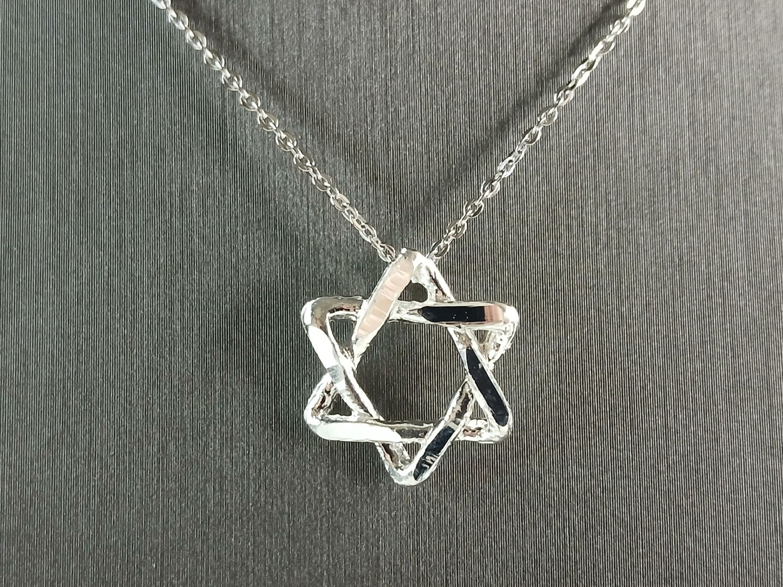 Sterling Silver Star of David Jewish Judaica Pendant Necklace: A STERLING SILVER STAR OF DAVID MODERNIST STYLE PENDANT WITH NECKLACE. PENDANT WITH NECKLACE WEIGHS 3.7g. PENDANT MEASURES 5/8" WIDE BY 5/8" LONG. THE NECKLACE MEASURES 18" LONG, ADJUSTABLE TO 16"