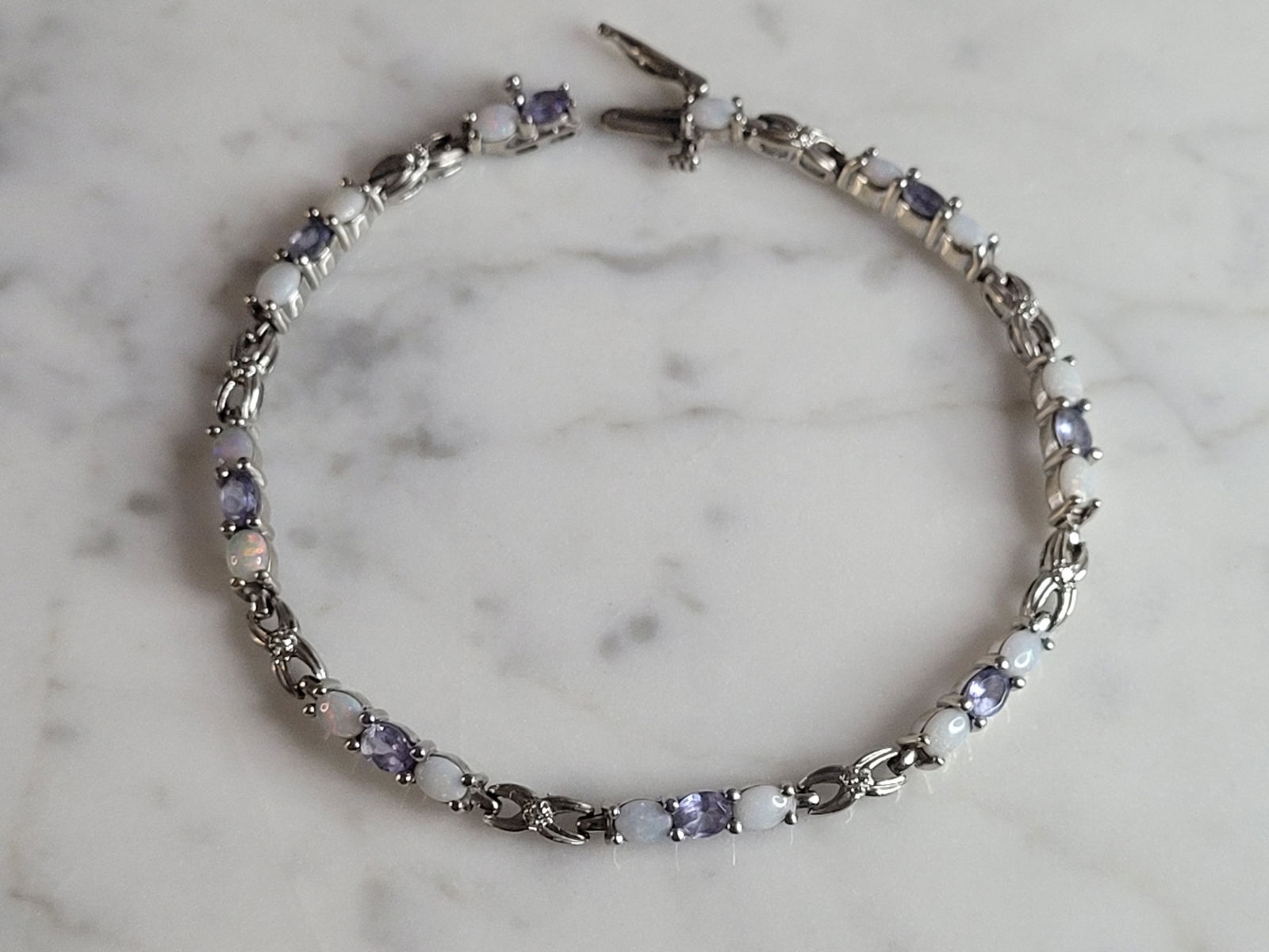 Womens Vintage Estate 10K Gold Opal Tanzanite Tennis Bracelet: A WOMENS VINTAGE ESTATE 10K WHITE GOLD OPAL & TANZANITE TENNIS BRACELET. THE BRACELET MEASURES 7 1/4" LONG BY 1/8" WIDE, AND WEIGHS 7.7g. NOT SURE IF THE STONES ARE REAL OR MAN MADE. WOULD MAKE A GREA