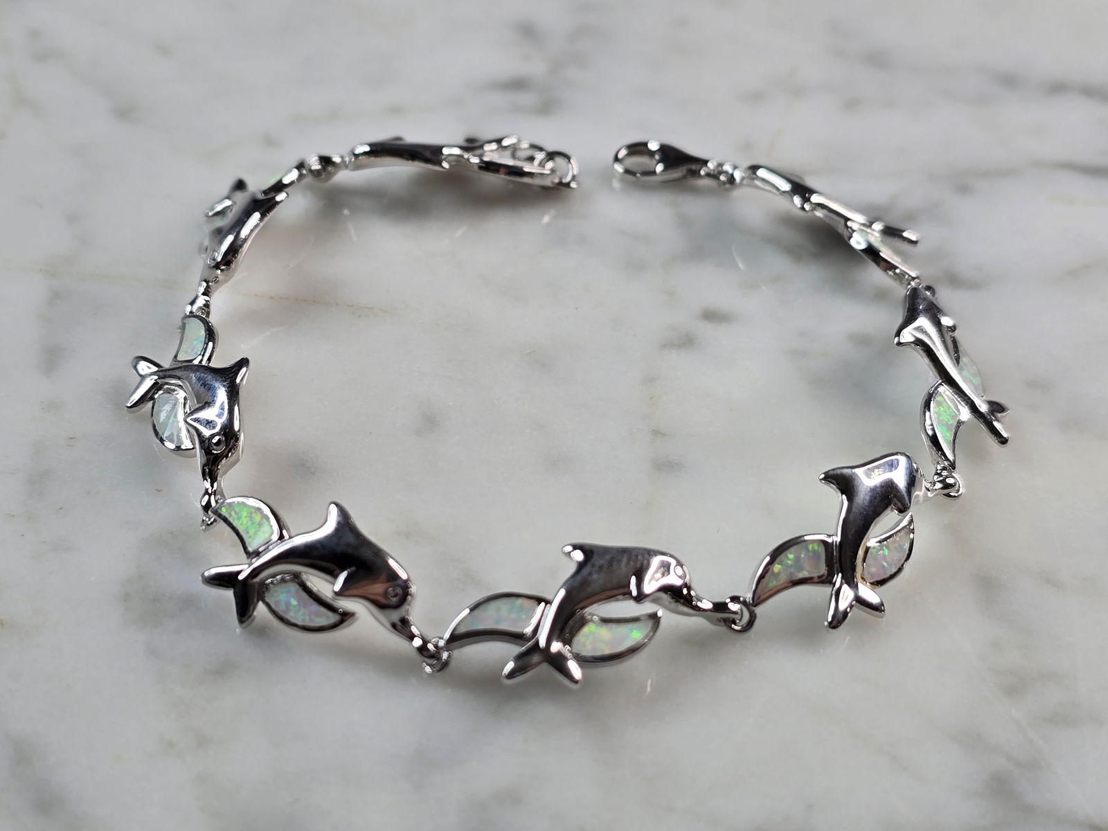 Womens Sterling Silver Opal Dolphin Bracelet: A WOMENS STERLING SILVER MODERNIST OPAL COLORED DOLPHIN BRACELET. THE BRACELET WEIGHS 12.0g AND MEASURES 7 7/8" LONG BY 1/2" WIDE. NOT SURE IF OPAL IS NATURAL OR MAN MADE. ANY QUESTIONS PLEASE DO NOT