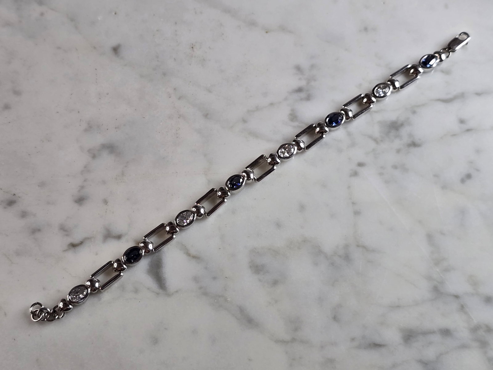 Womens Vintage Estate Sterling Silver Modernist Sapphire Bracelet: A WOMENS VINTAGE ESTATE STERLING SILVER MODERNIST TENNIS BRACELET WITH DARK SAPPHIRE COLORED STONES. NOT SURE IF THE STONES ARE NATURAL OR MAN MADE. THE BRACELET MEASURES 7 1/2" LONG BY 1/4" WIDE, AND