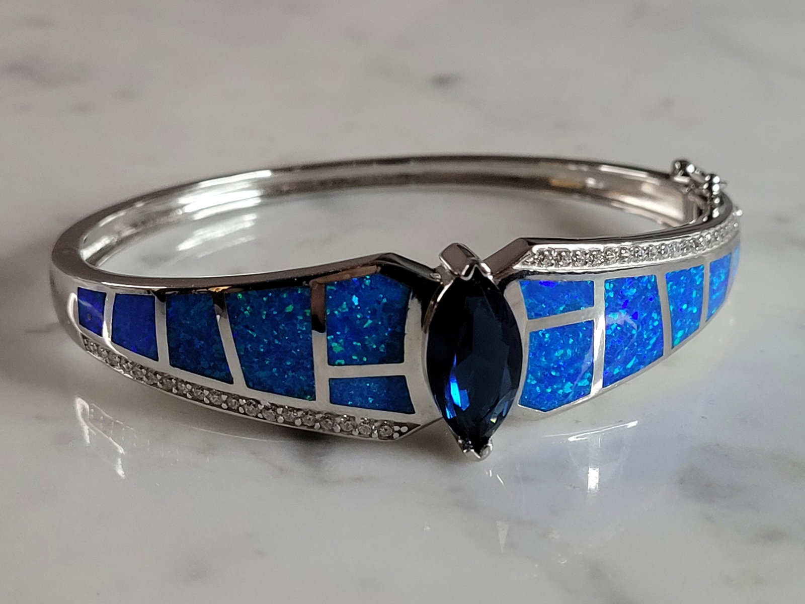 Womens Sterling Silver Modernist Blue Opal Bangle Bracelet: A WOMENS STERLING SILVER MODERNIST BLUE OPAL BANGLE BRACELET WITH A SAPPHIRE COLORED STONE. THE BRACELET WEIGHS 25.5g AND IS ABOUT 5/8" WIDE. THE CIRCUMFERENCE IS 6 3/4". NOT SURE IF THE OPAL IS REAL 