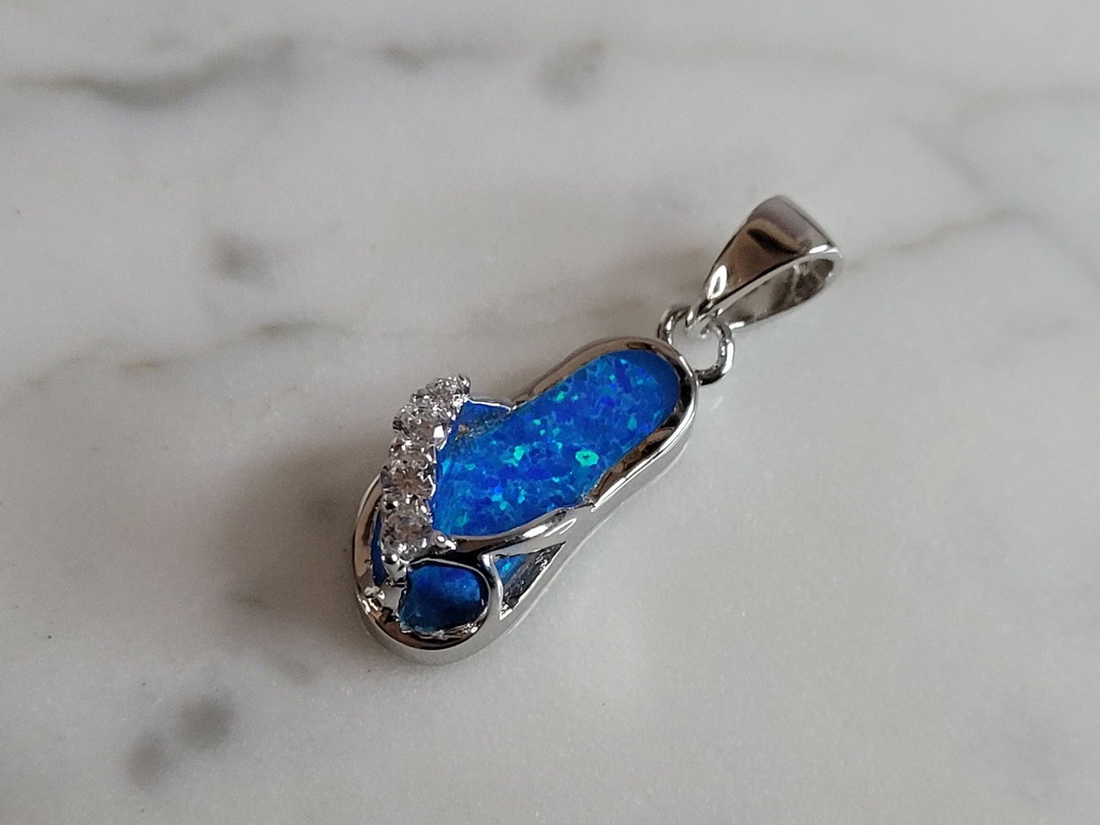 Womens Sterling Silver Blue Opal Sandal Flip Flop Pendant: A WOMENS STERLING SILVER BLUE OPAL SANDAL OR FLIP FLOP PENDANT. NOT SURE IF STONES ARE REAL OR MAN MADE. THE PENDANT WEIGHS 2.4g AND MEASURES 1" LONG BY 1/4" WIDE. MAKES A GREAT GIFT FOR THAT SOMEONE 