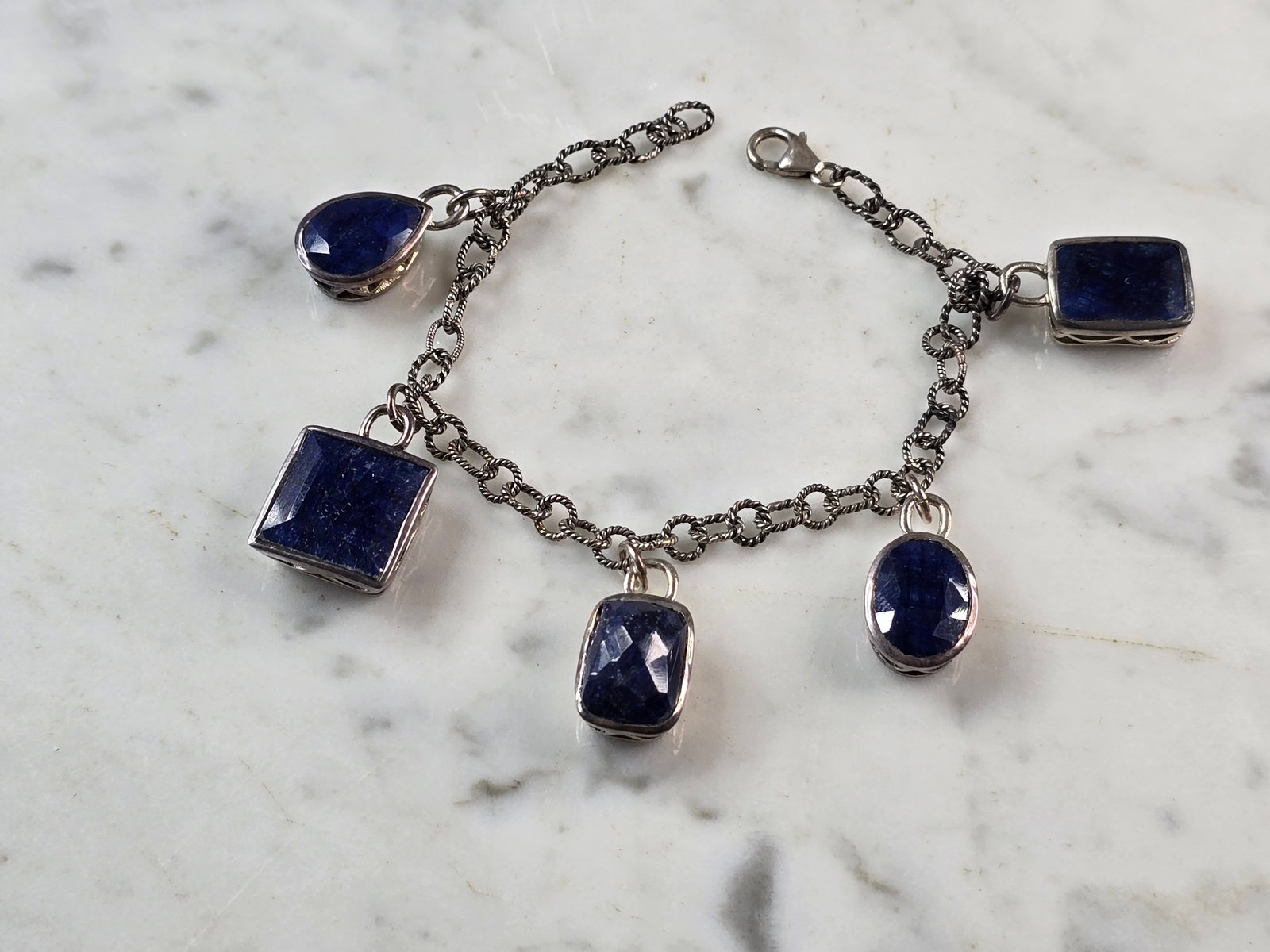 Womens Vintage Sterling Silver Modernist Sapphire Charm Bracelet: A WOMENS VINTAGE ESTATE STERLING SILVER MODERNIST CHARM BRACELET WITH NATURAL BLUE SAPPHIRE COLORED STONES. THE BRACELET MEASURES 7 1/2" LONG BY 3/16" WIDE, AND WEIGHS 25.7g. NOT SURE IF THE STONES AR
