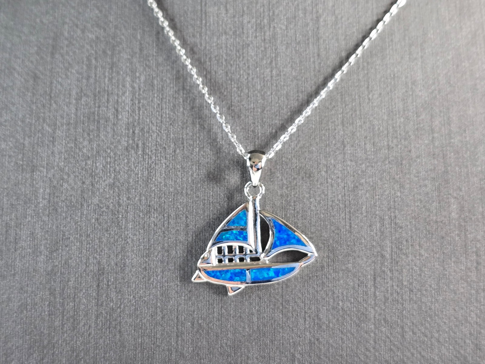 Womens Sterling Silver Blue Opal Sailboat Pendant Necklace: A WOMENS STERLING SILVER BLUE OPAL SAIL BOAT PENDANT WITH NECKLACE. THE PENDANT WITH NECKLACE WEIGHS 5.0g. THE PENDANT MEASURES 7/8" LONG BY 7/8" WIDE, AND THE NECKLACE MEASURES 18" LONG, ADJUSTABLE T