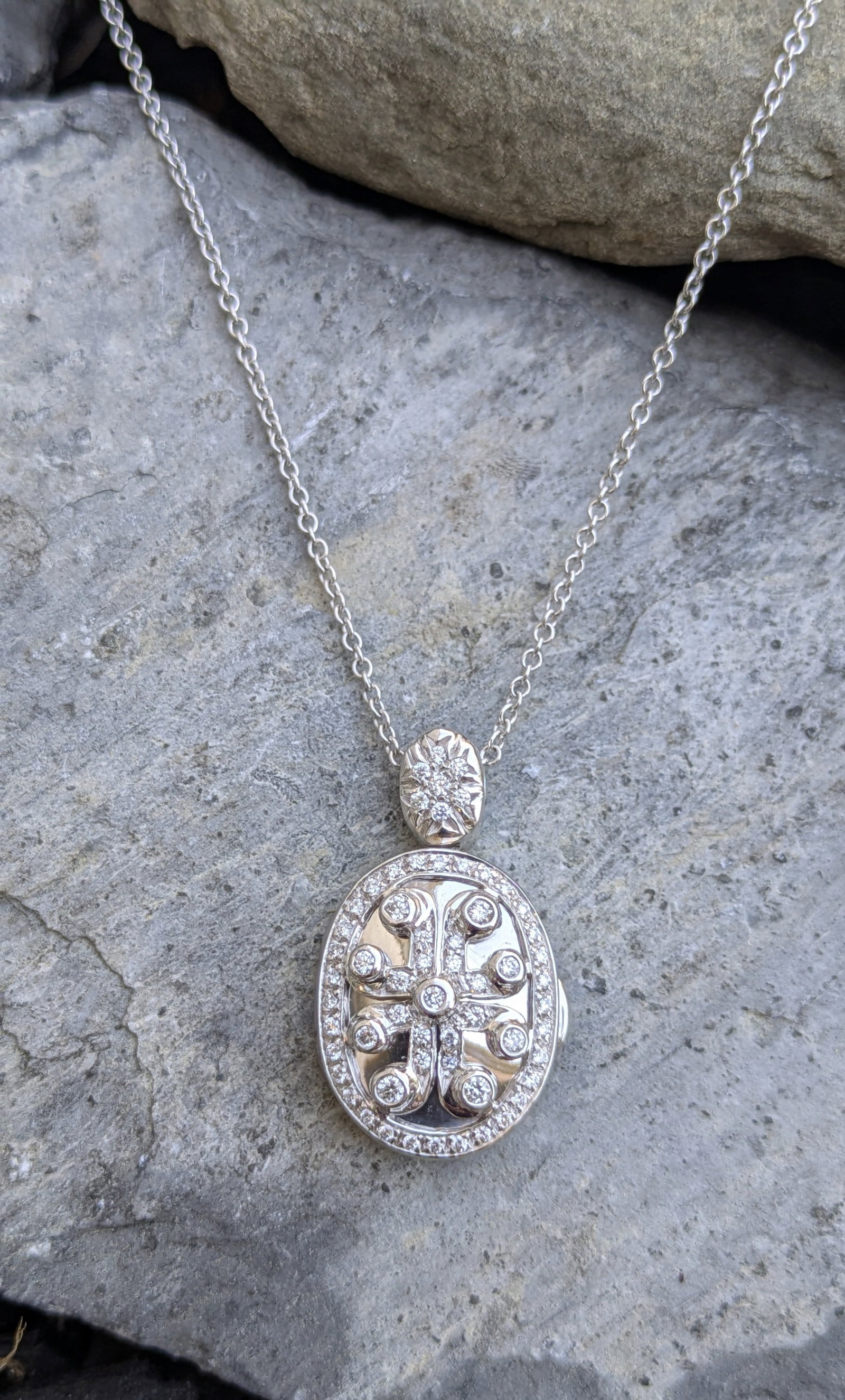 Diamond Locket Pendant: Crafted in 18k white gold featuring (62) round diamonds weighing approximately .60cttw. The locket measures 1 1/4in x 3/4in and comes with a chain measuring 18in and crafted in 14k white gold. The tot